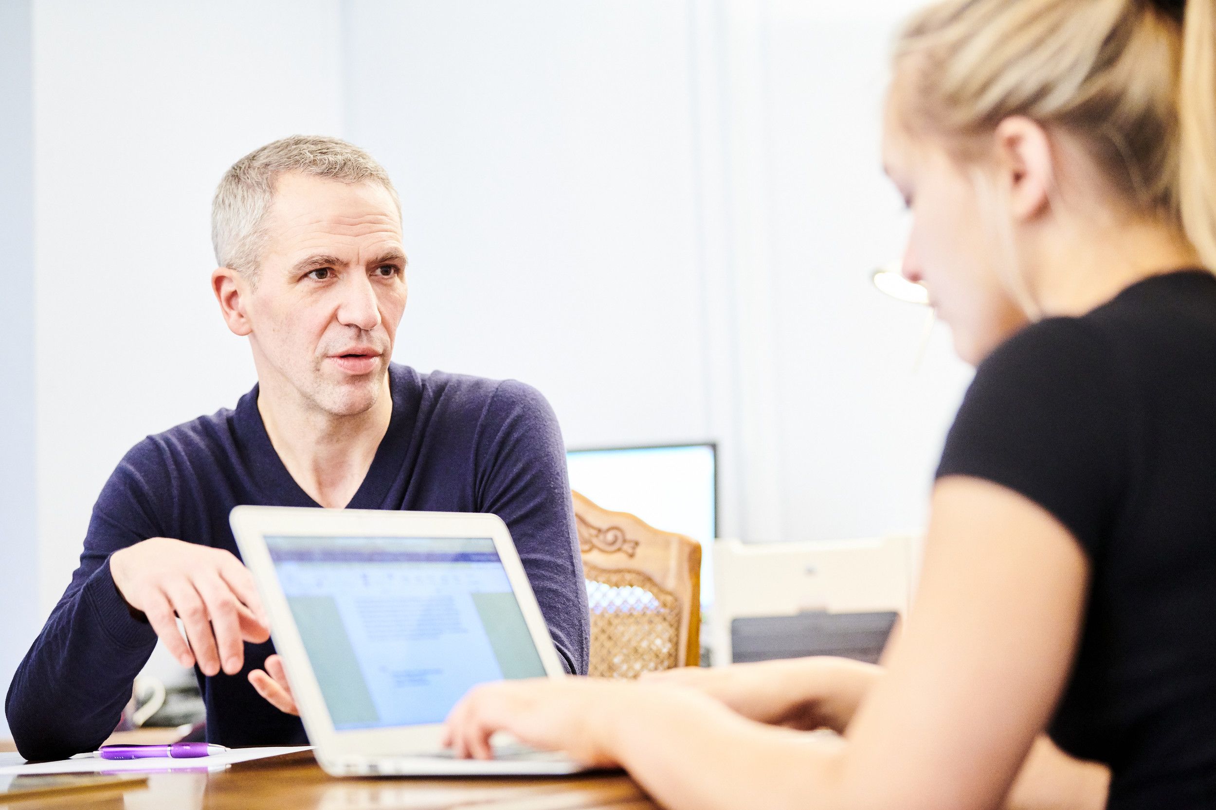 Two individuals talking and typing on a laptop