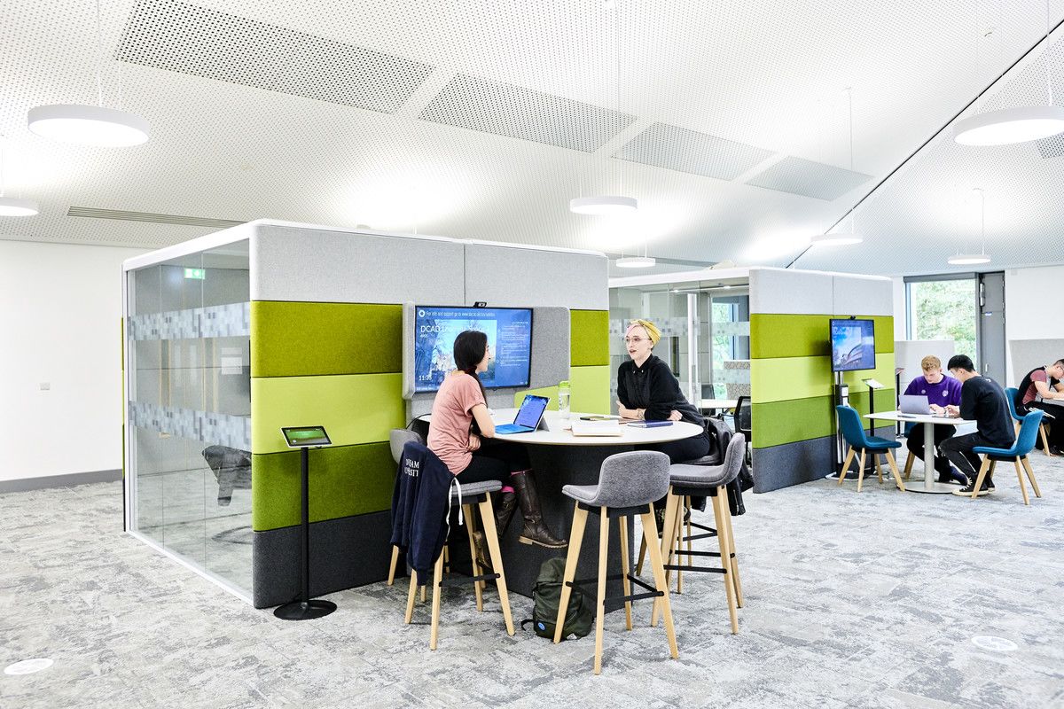 Two students sitting at a high table with a screen next to them