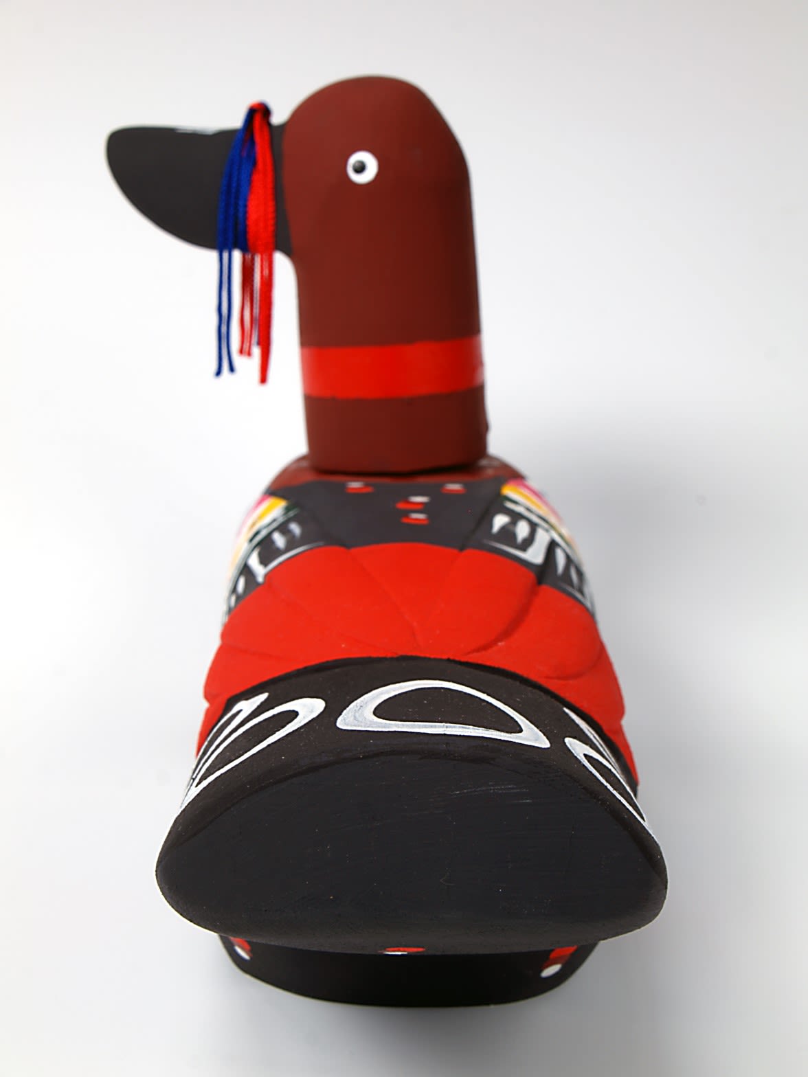 Red and black painted wooden wedding duck. The duck has a red and blue ribbon around it's beak. The wings have patterns with yellow and pink stripes and red and white spots.