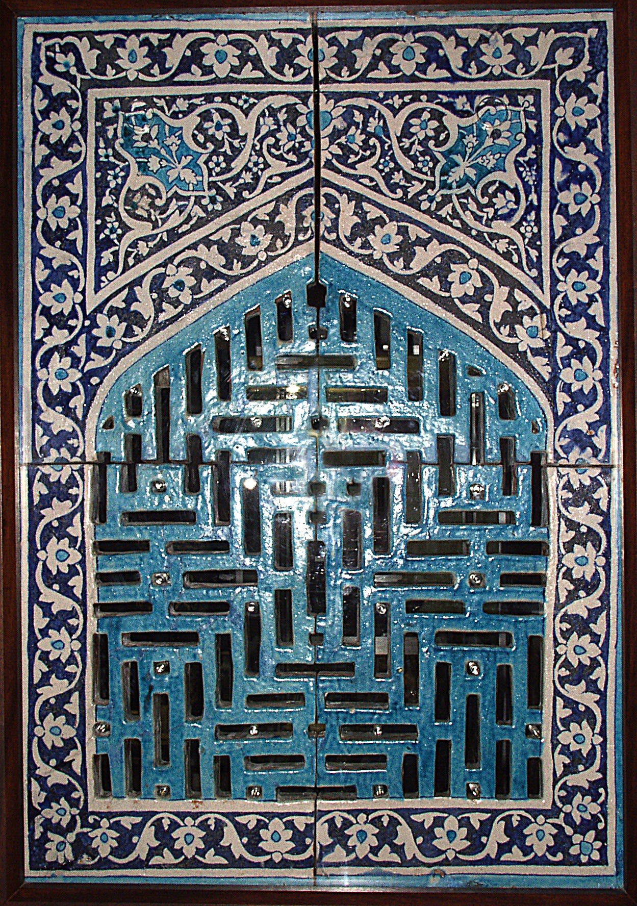 Blue and faded orange window grill, cut with rectangular patterns and a surrounding floral border.