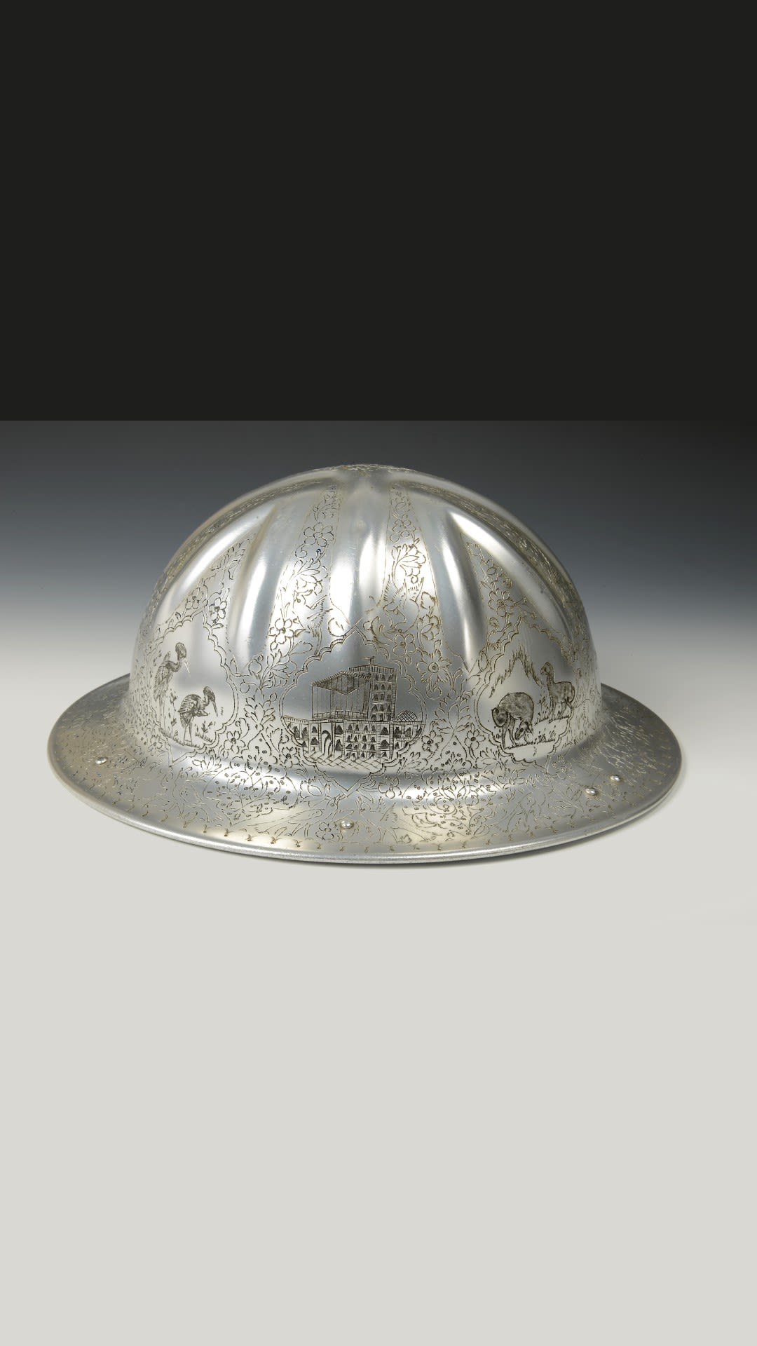 Shiny silver helmet, carved with patterns of birds and mammals, as well as buildings, leaves and flowers.