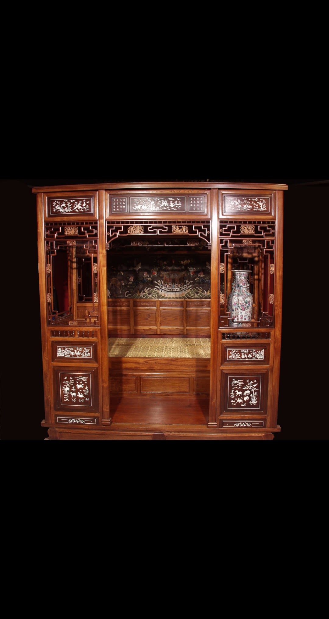 A large and ornate Chinese bed, with a wooden frame surrounding the sleeping area. The frame is painted with a pattern including animals and plants