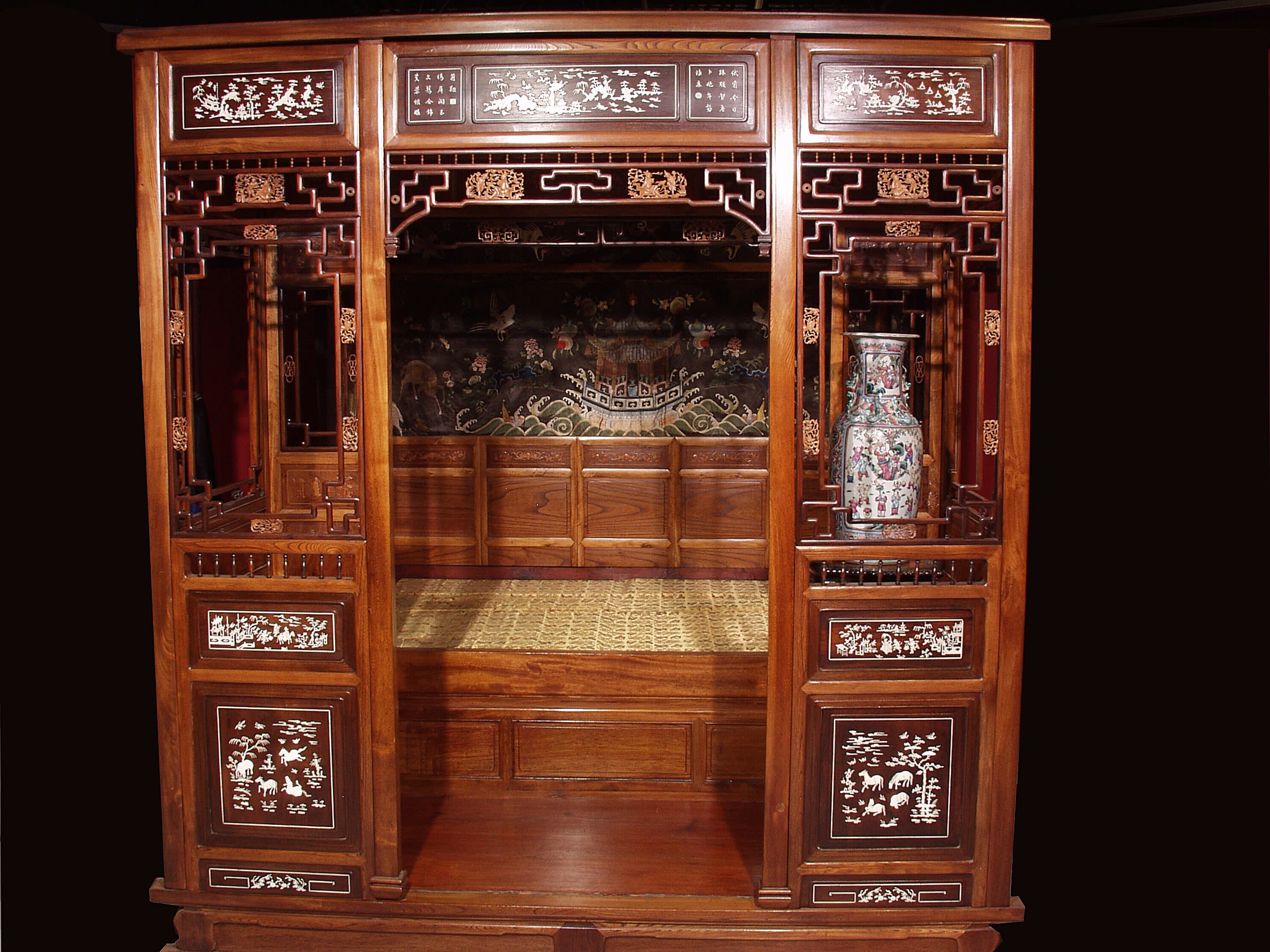 A large and ornate Chinese bed, with a wooden frame surrounding the sleeping area. The frame is painted with a pattern including animals and plants