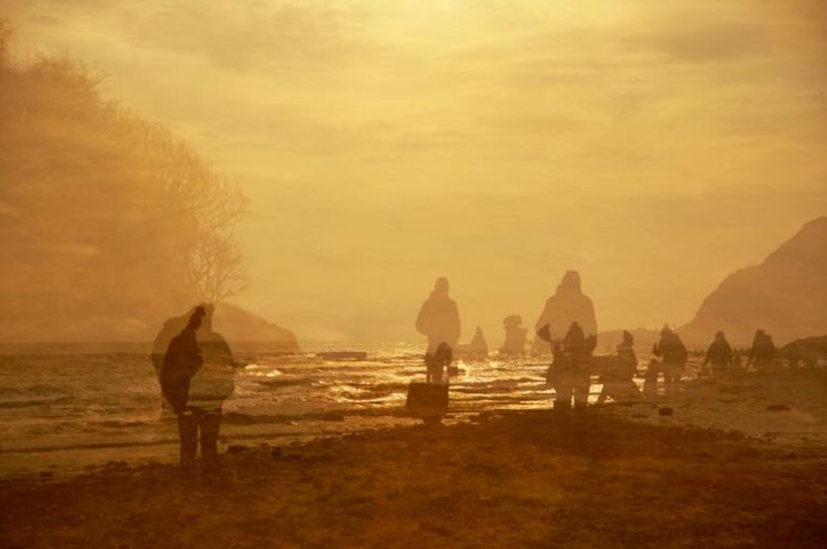 Double exposed photo of figures walking on a beach.