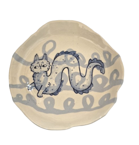 Ceramic white stoneware plate, with blue background looping pattern. On top a blue cat-like illustration of the Lambton Worm.