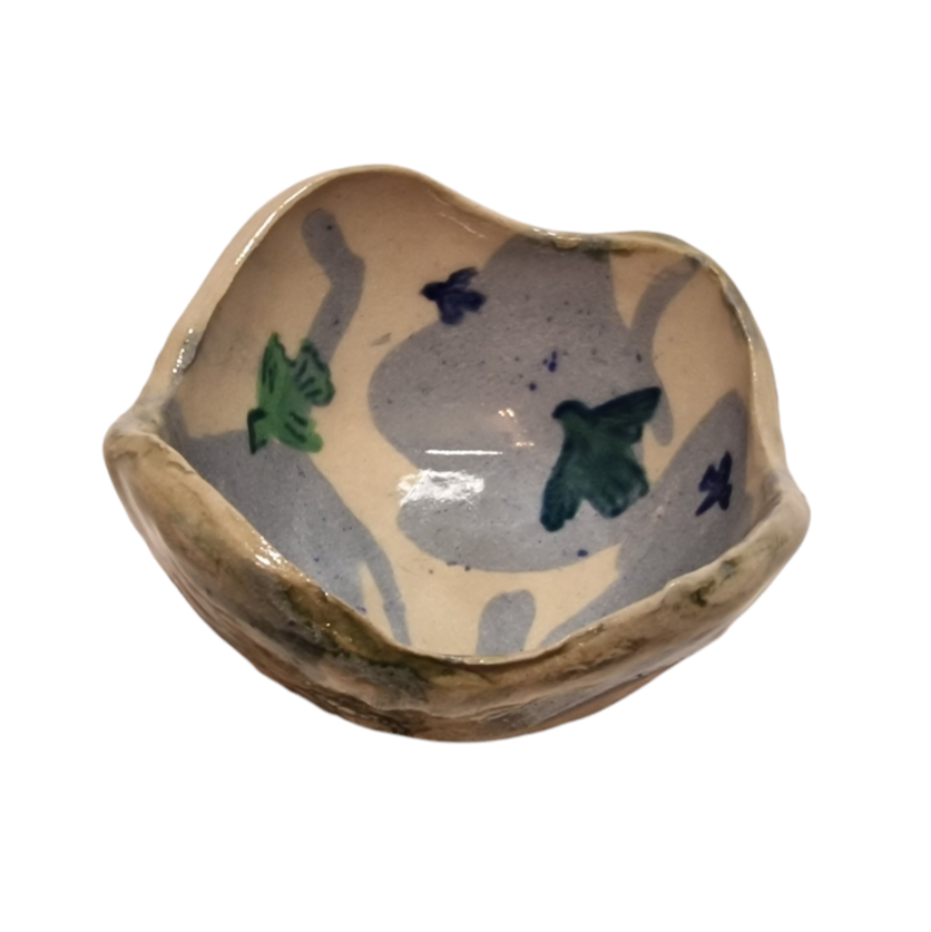 Above view of hump made stoneware bowl with green and blue birds flying over blue clouds