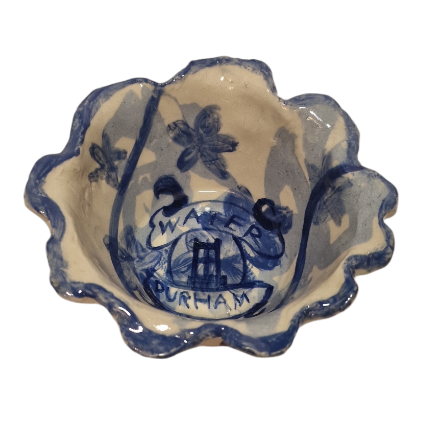 Above view of hump made stoneware bowl with blue illustration and ribbon banner writing reading: WATER DURHAM. Rim of bowl is wavey