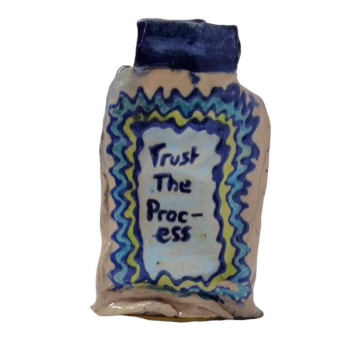 Hand built bottle with green and blue pattern. Text in center reads Trust The Process