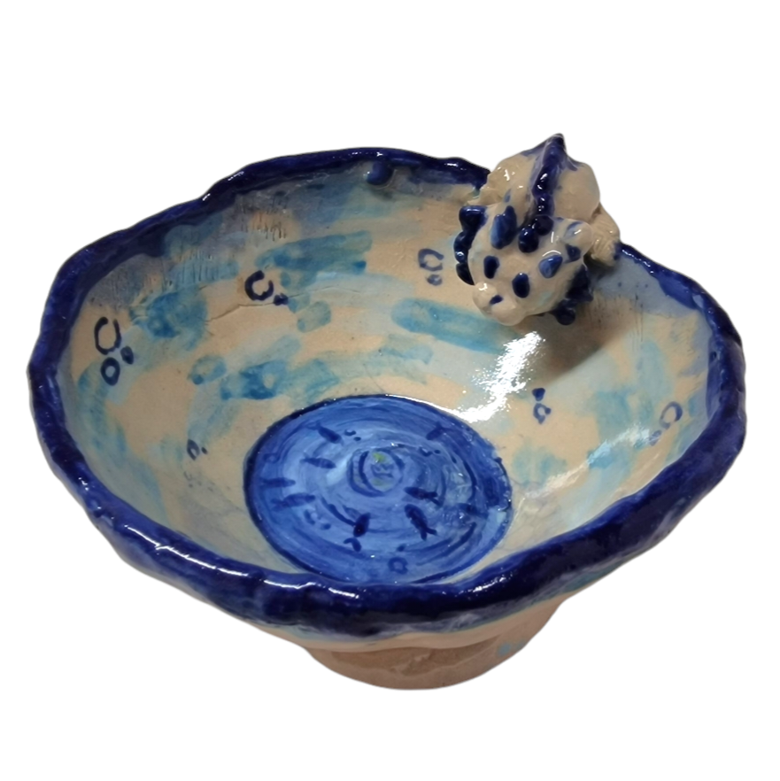 Above view of hump made stoneware bowl with pool like illustration in center with fishes. On the rim of the bowl a 3D model of a cat like creature looks at the water 