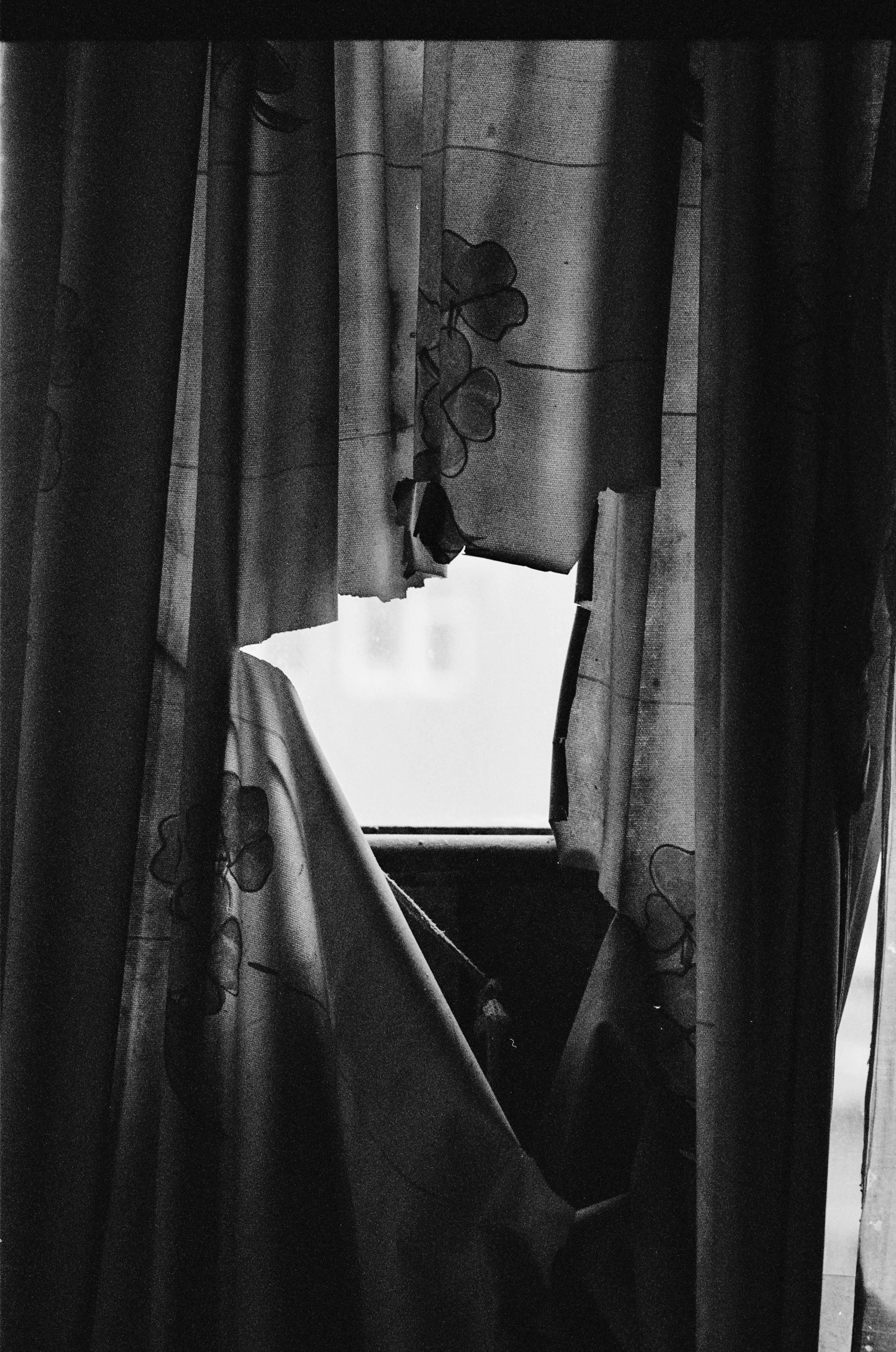 Black and white photo of a window with broken curtains