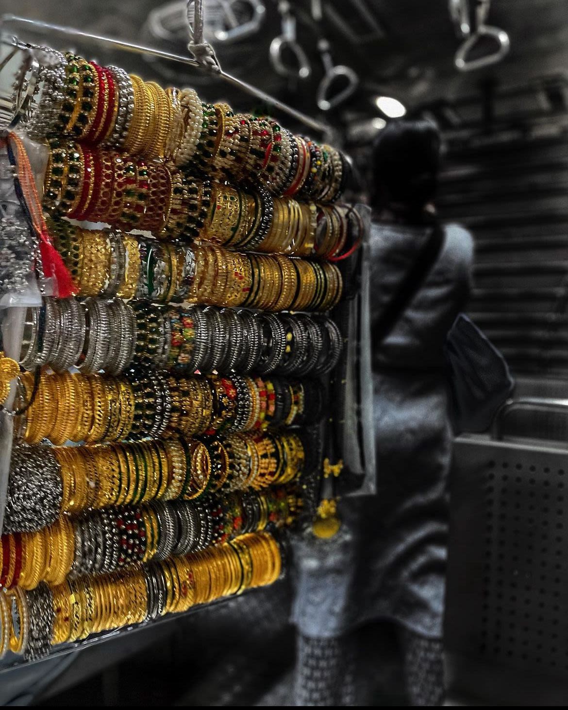 Close of photograph of golden bangles displayed in a market. The background and surrounding image is black and white, while the bangles are gold.
