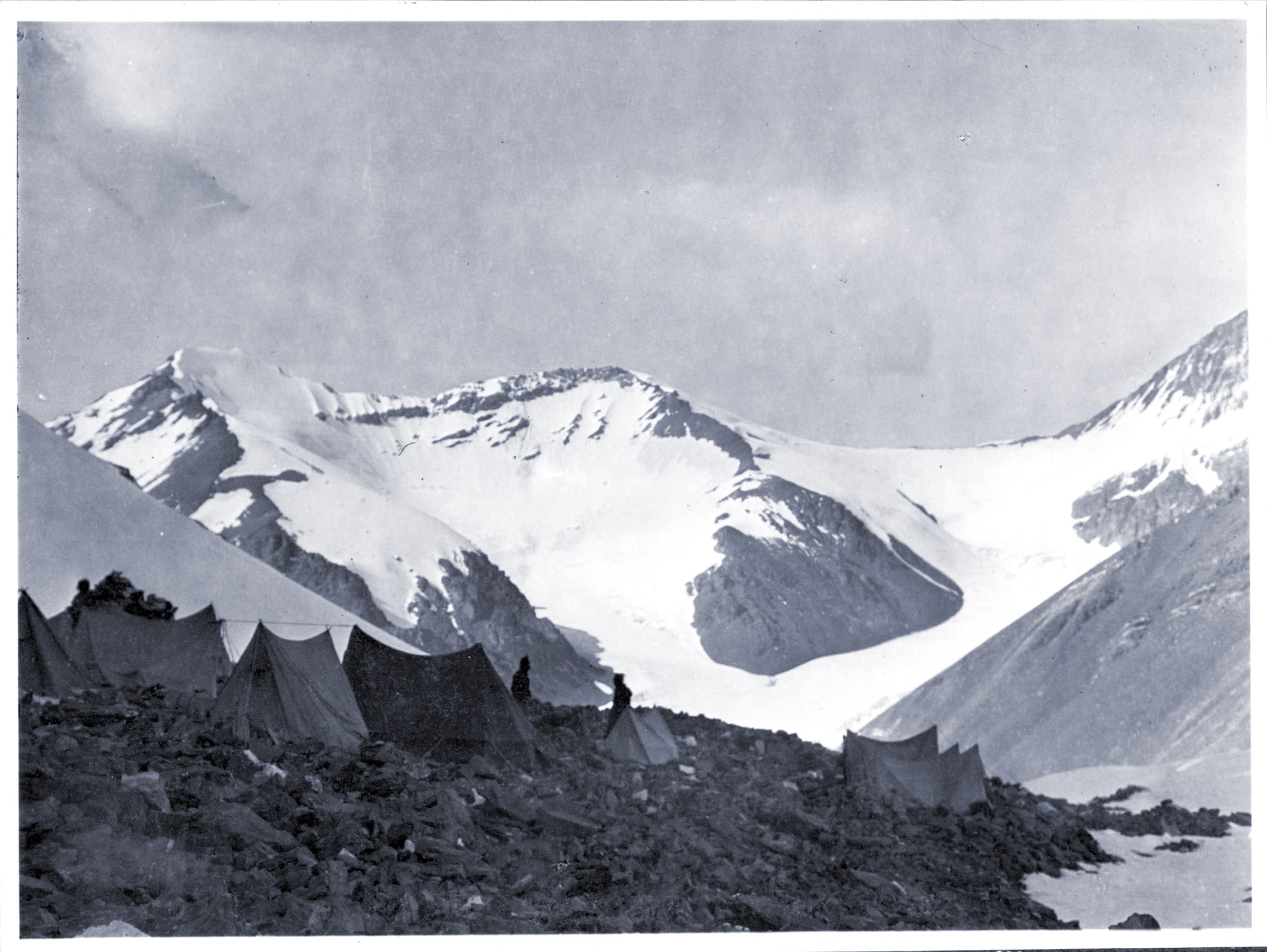 Several pitched tents in the foreground of a snowy mountainous landscape. Snow-covered peaks are visible in the background.