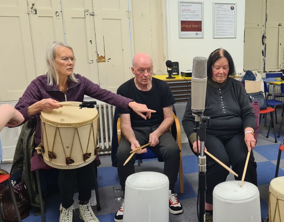 A group of three people sat playing drums.