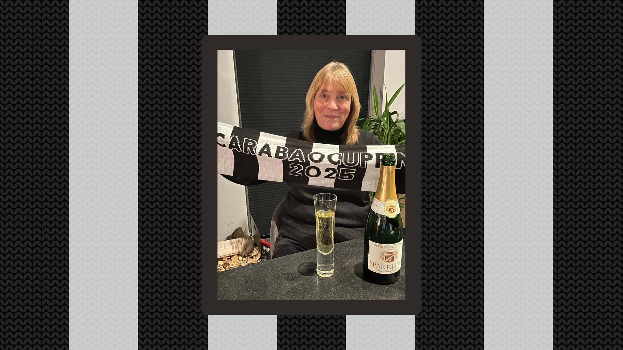 A Photo of Lynne at home with a glass of champagne, holding up a black and white scarf reading Carabao Cup Final 2025.