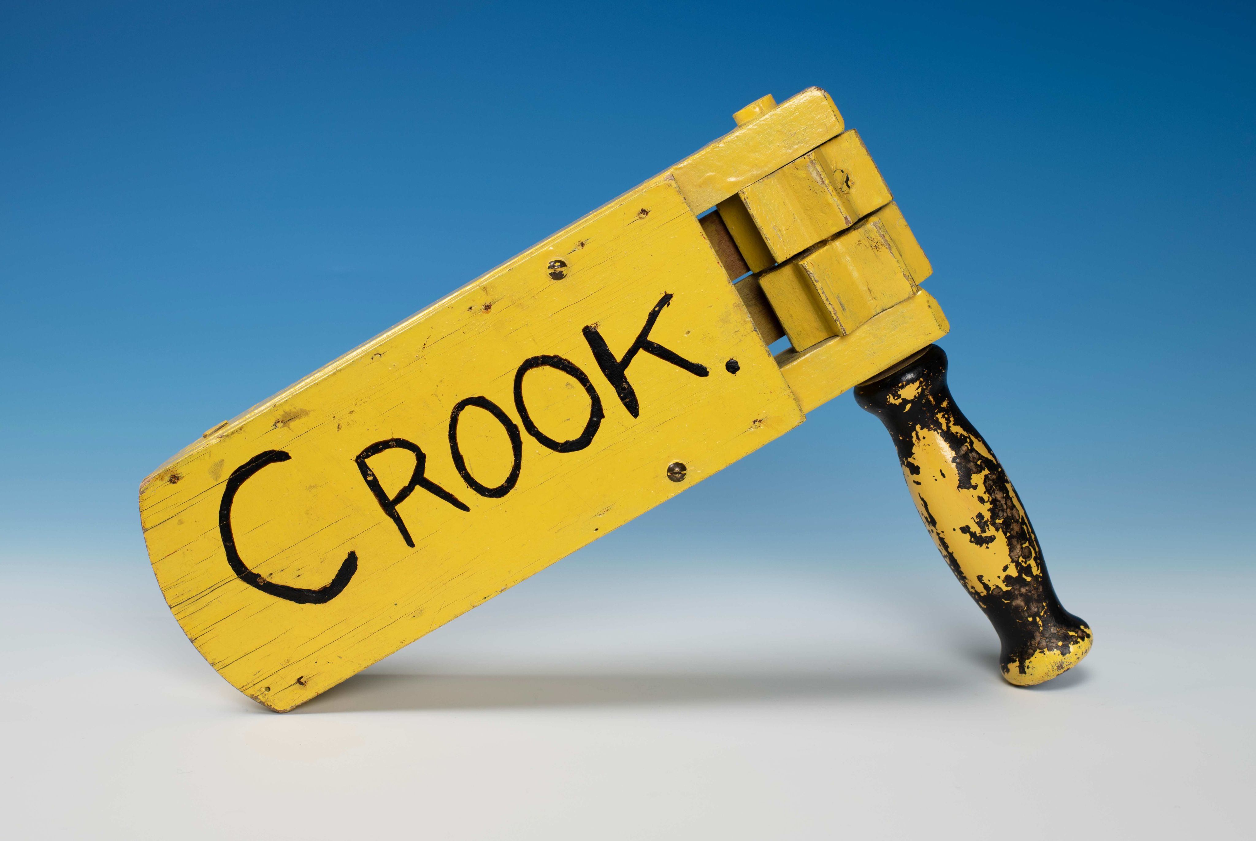 A yellow, wooden football supporter rattle with word 'Crook' written on it.