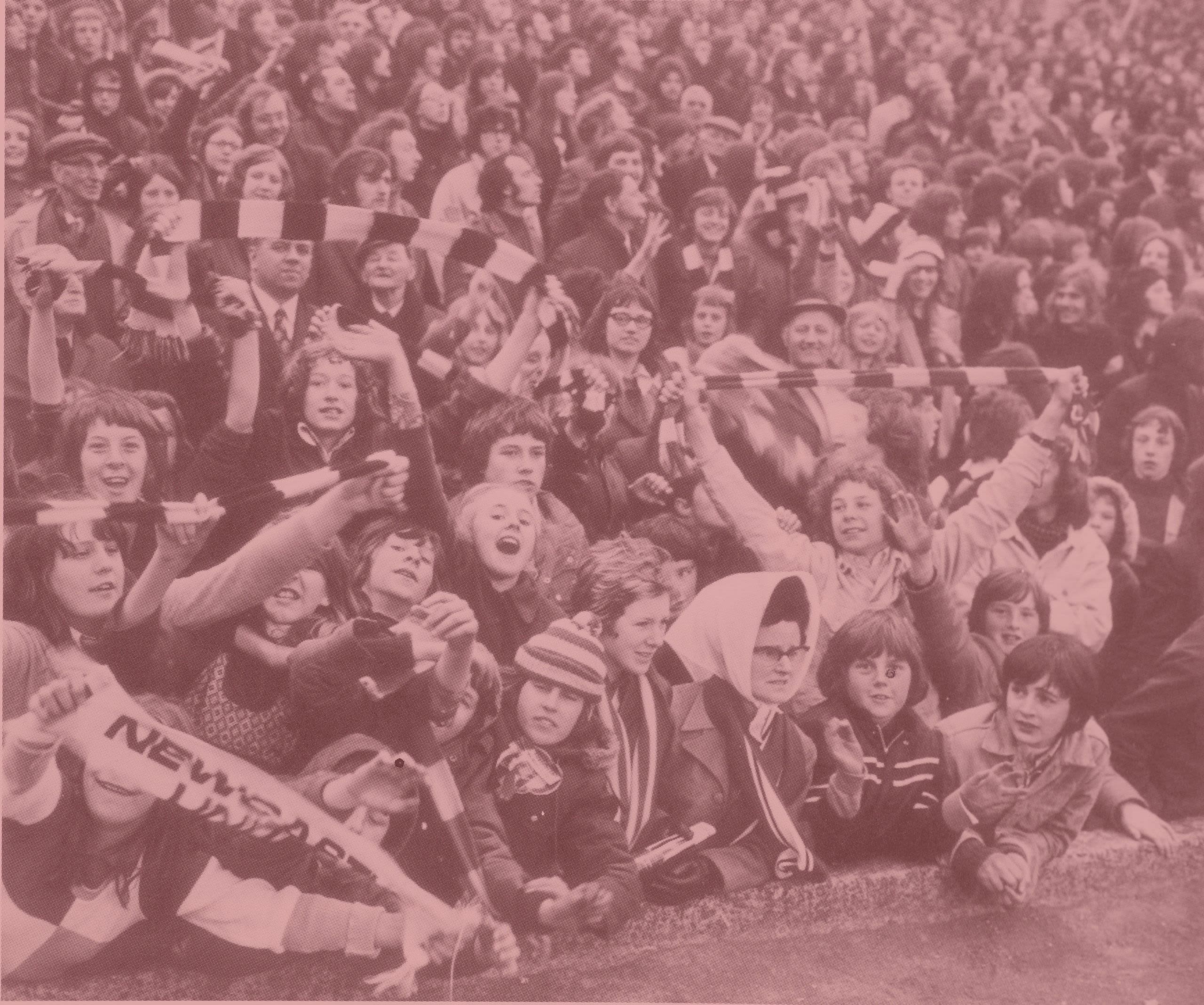 Black and white photo of football fans holding striped scarves aloft. A woman wearing glasses and a large white bonnet sits prominently in the centre of the photo.