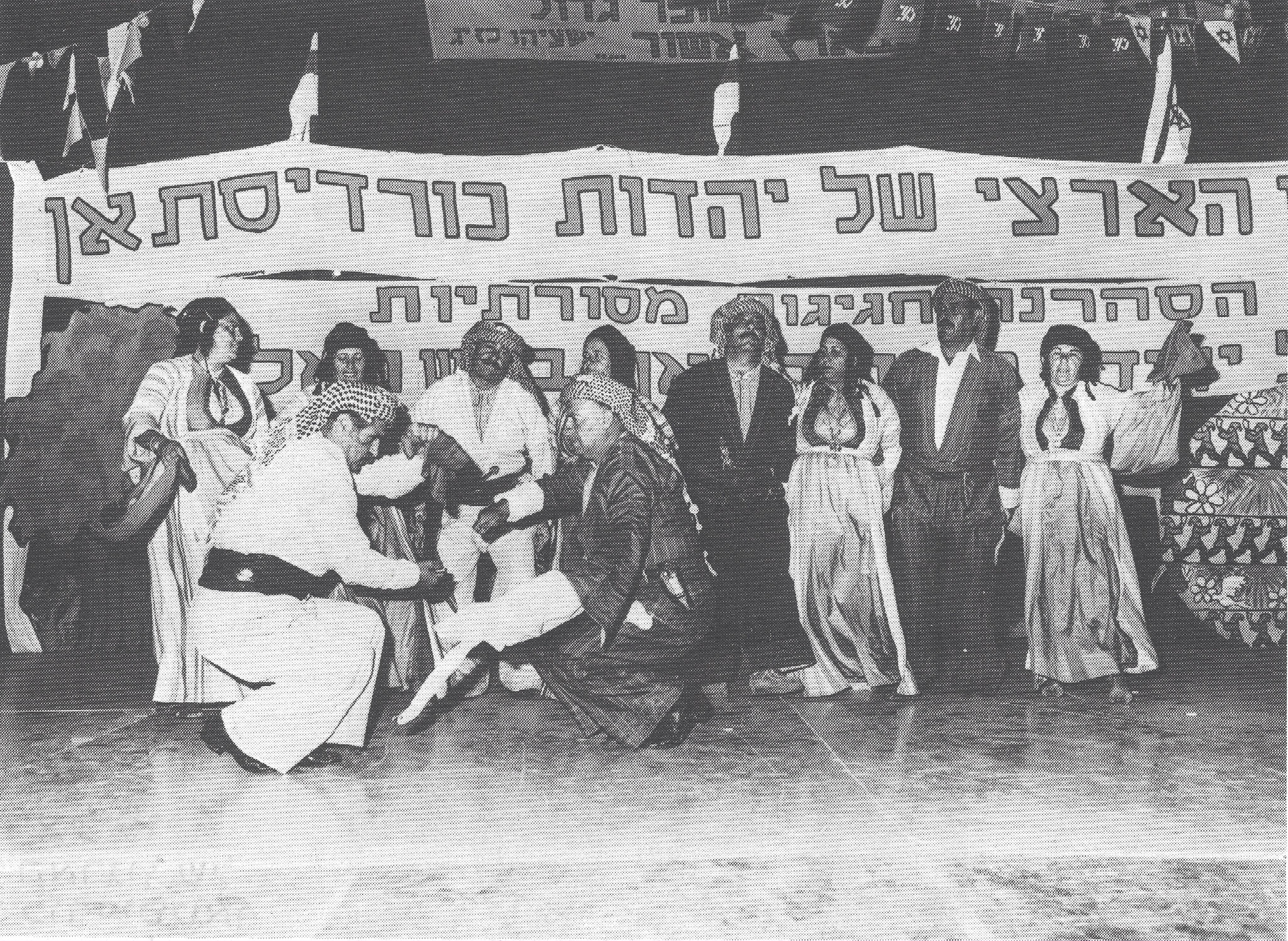 Black and white photograph of two people dancing in the foreground, a line of people dancing in the middle ground, and a banner in the background.