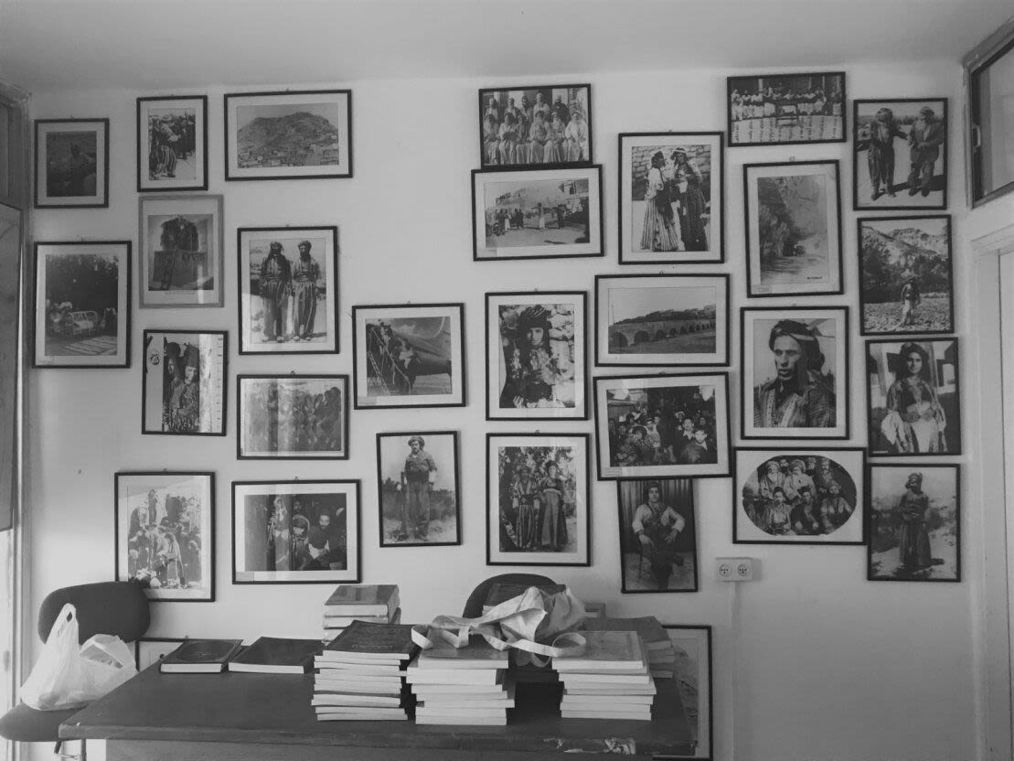 Black and white photographs, indoors, desk and wall full of old photographs.
