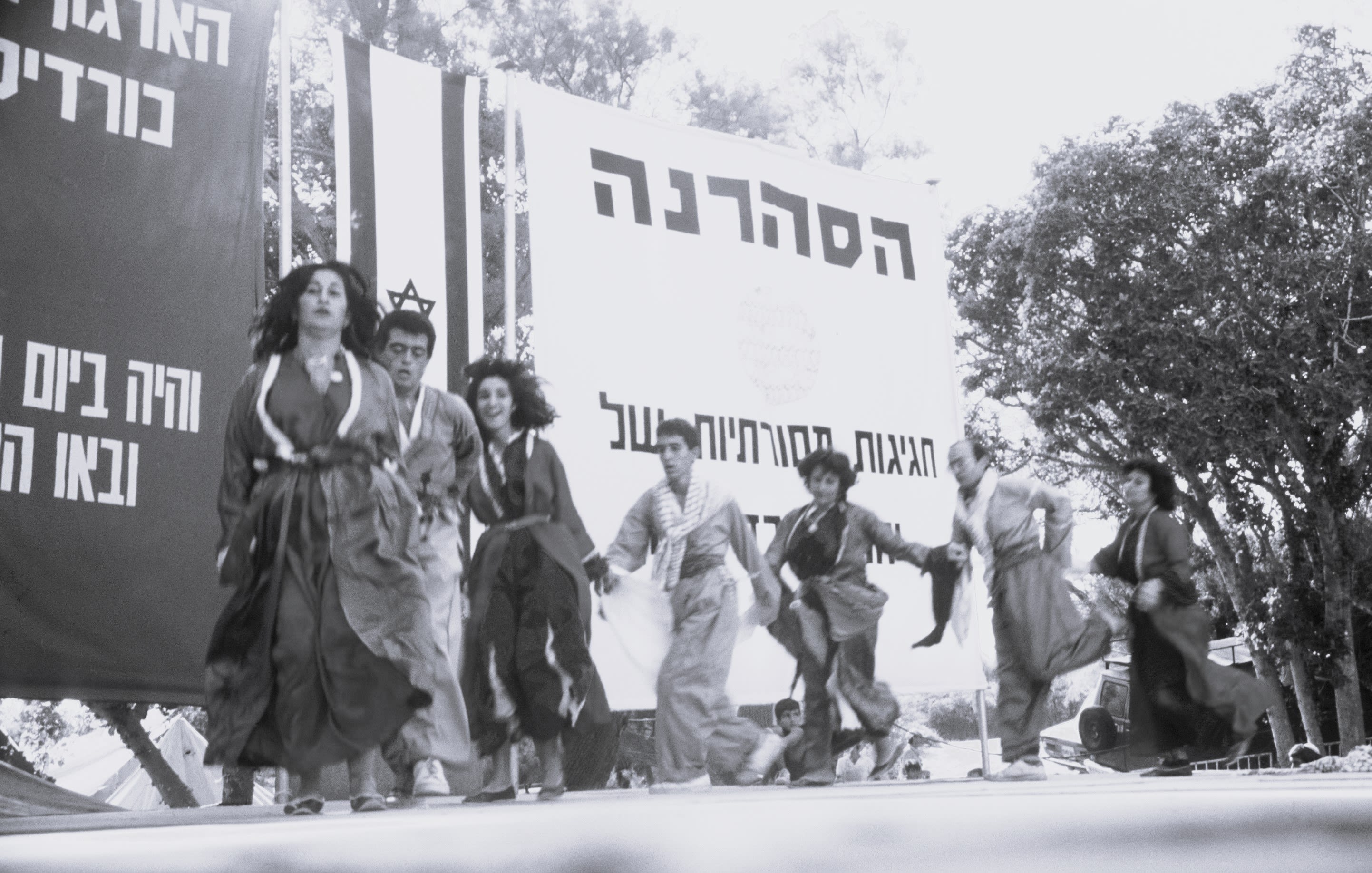 Black and white photograph of seven people holding hands and dancing.