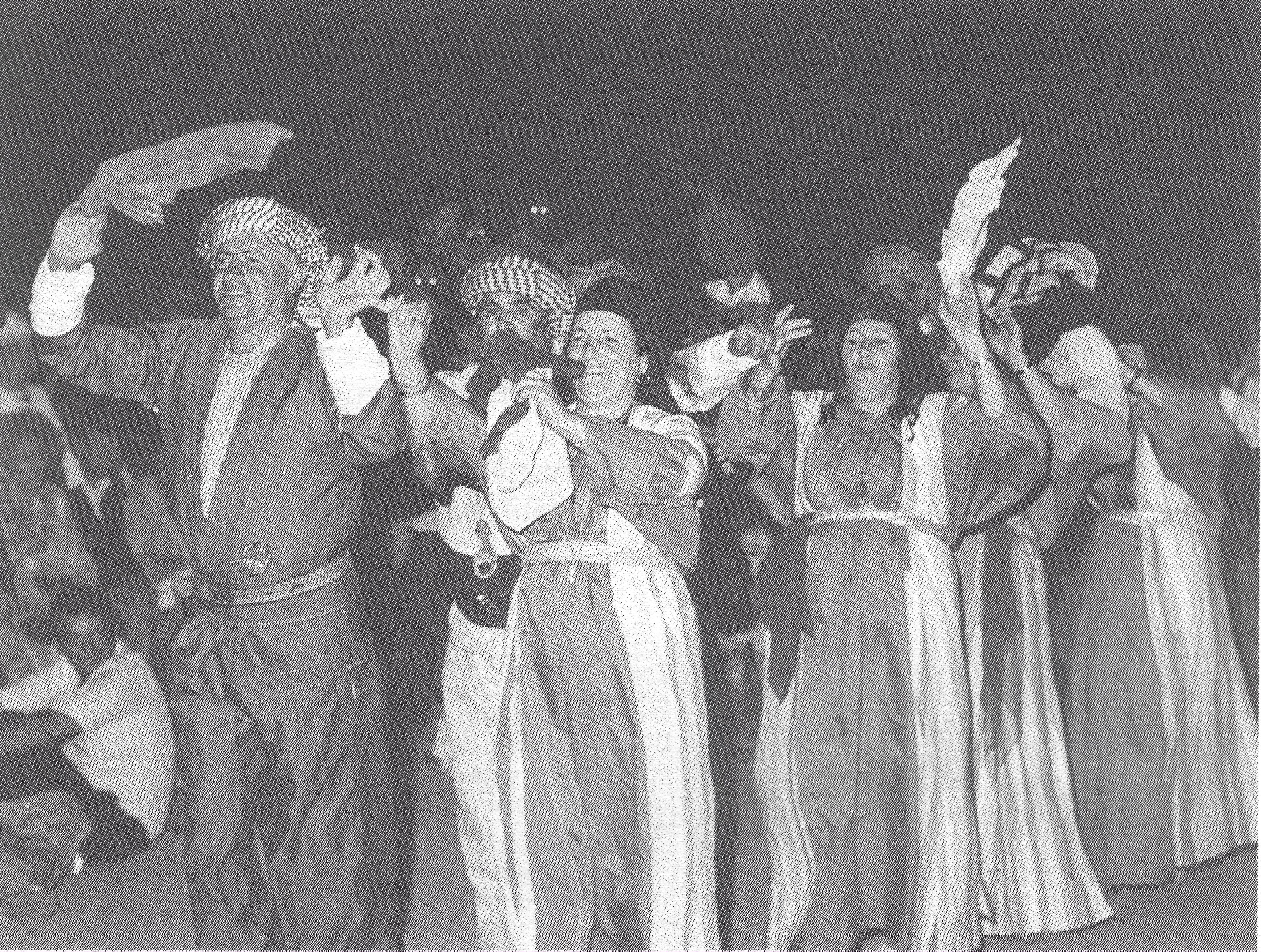 Black and white photograph of a group of people dancing with their hands up waving scarf.