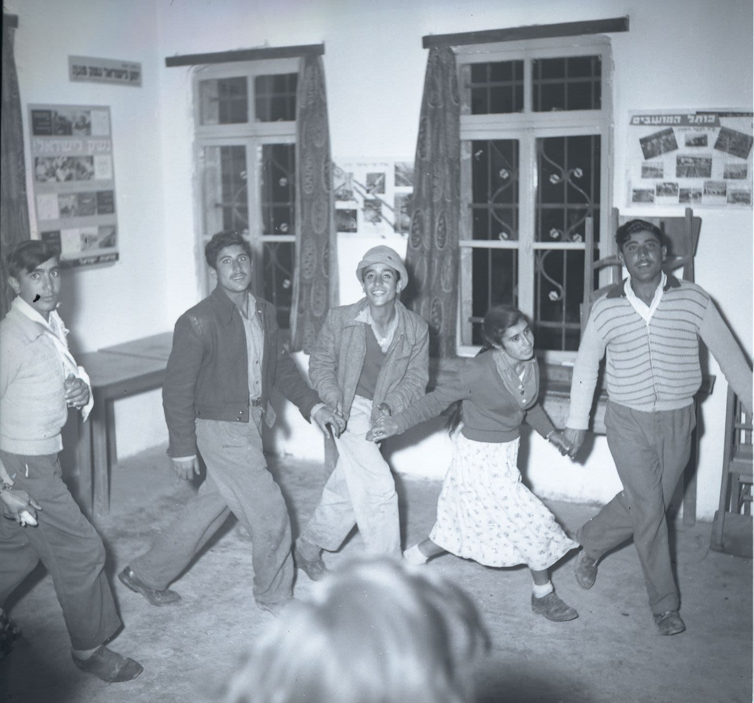 Black and white photograph of five people dancing holding hands.