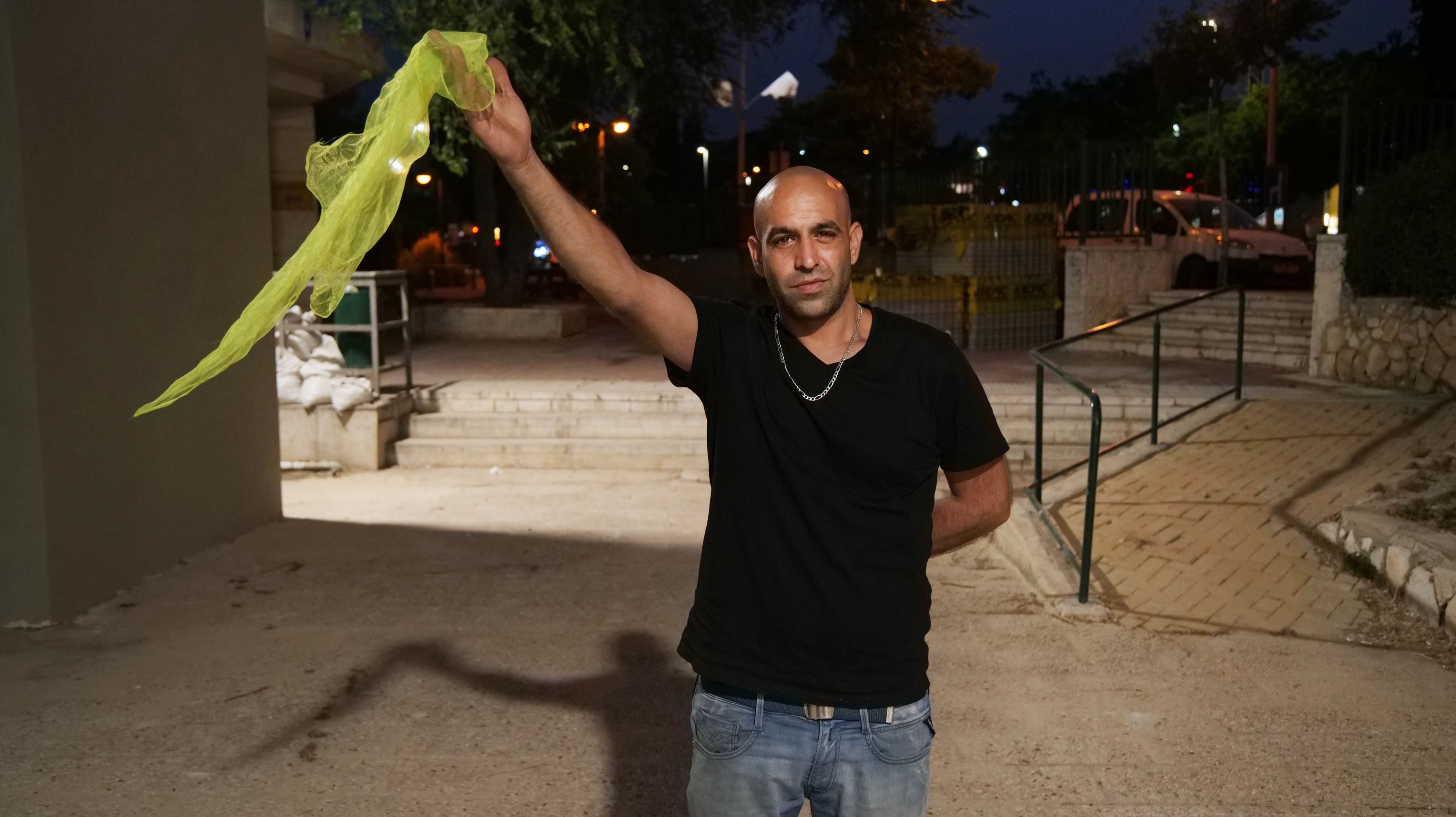 Colour photograph, outdoors, man waving yellow silk scarf.