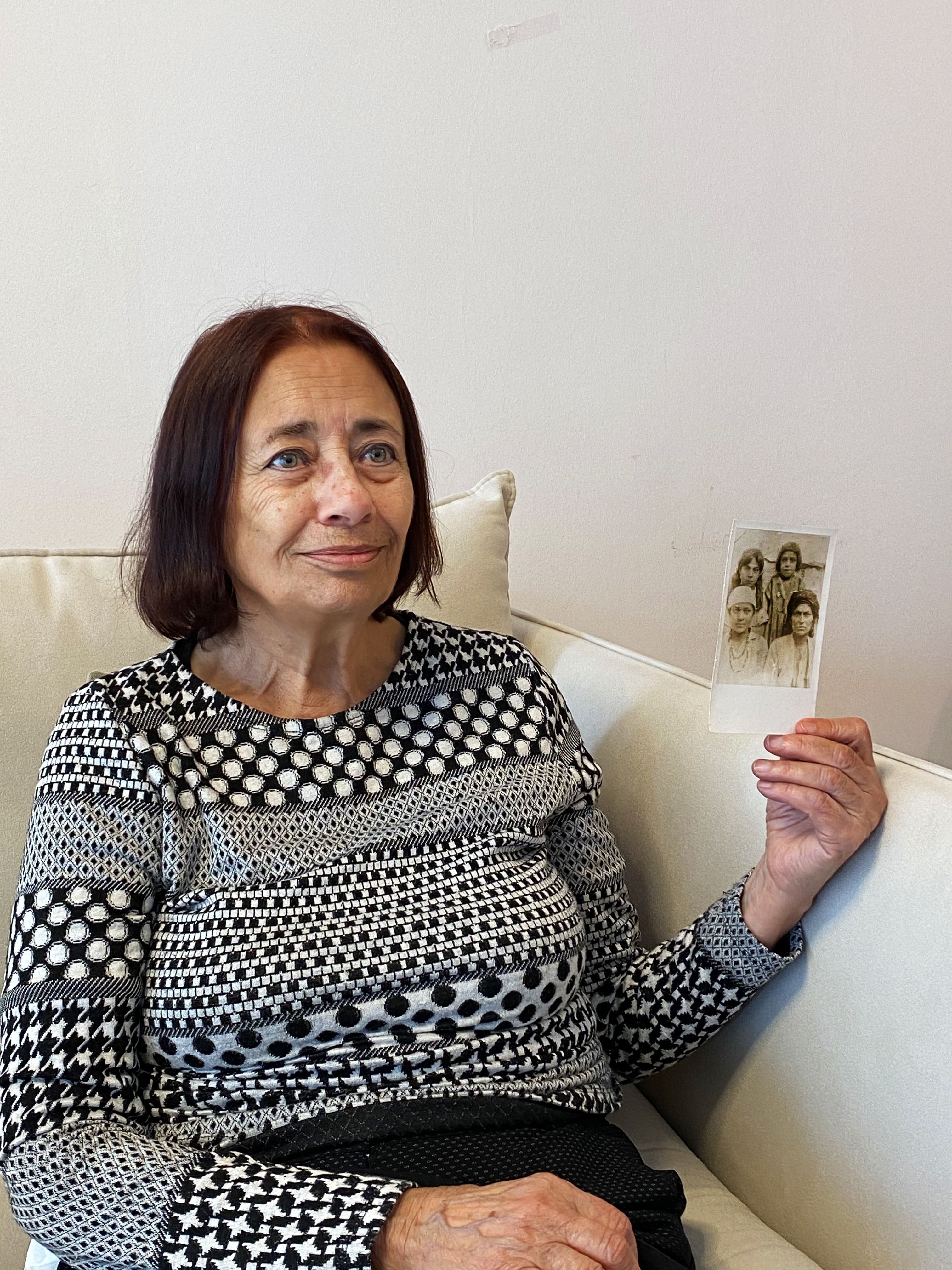 Colour photograph, indoors, woman holding up a family photograph of four people.