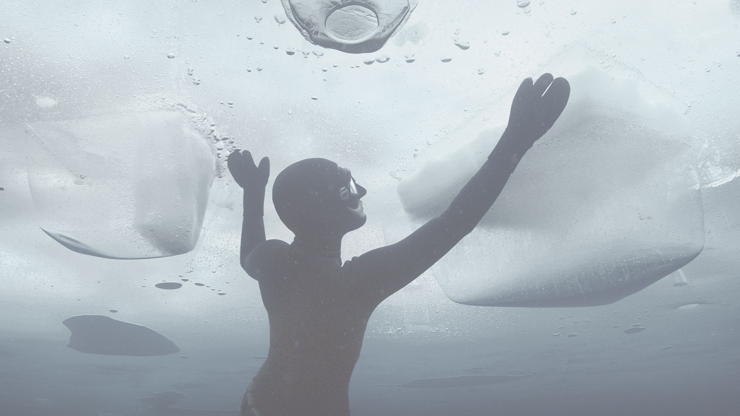 A diver under a sheet of ice reaches for the surface