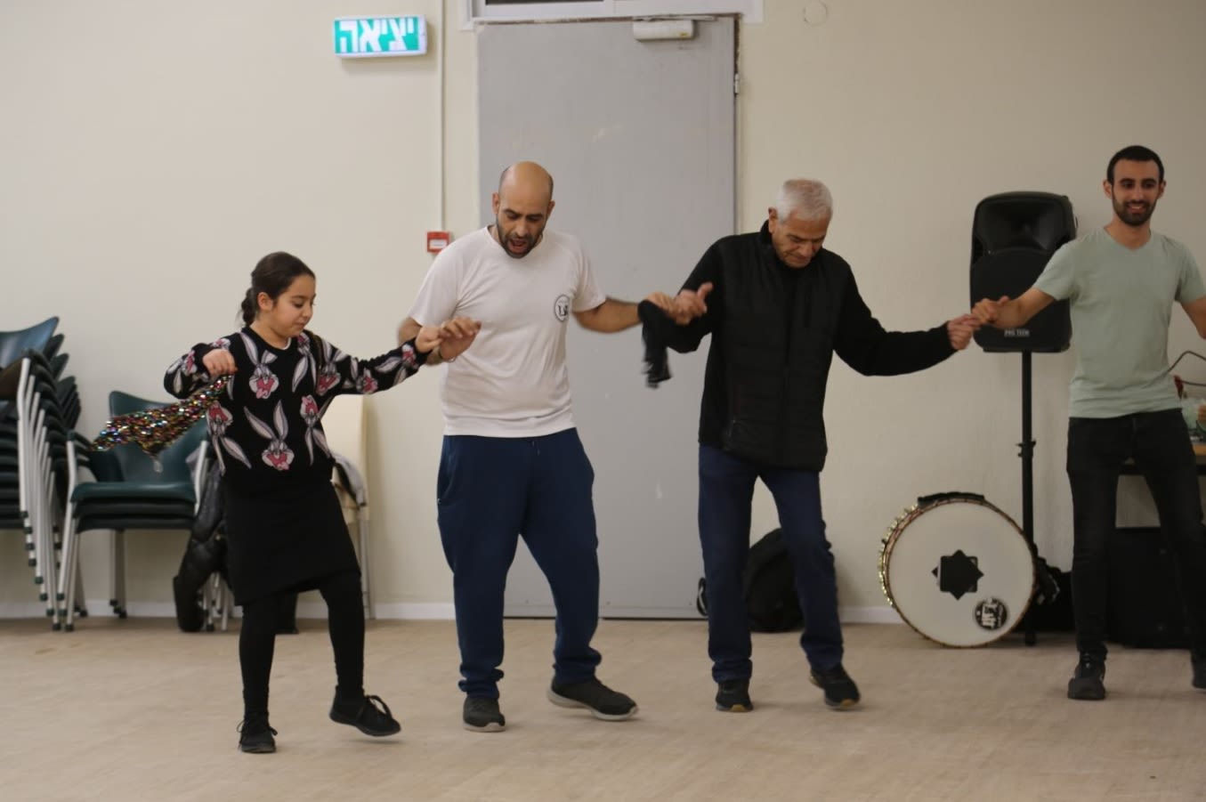 Colour photograph, indoors, of four people holding hands and dancing.