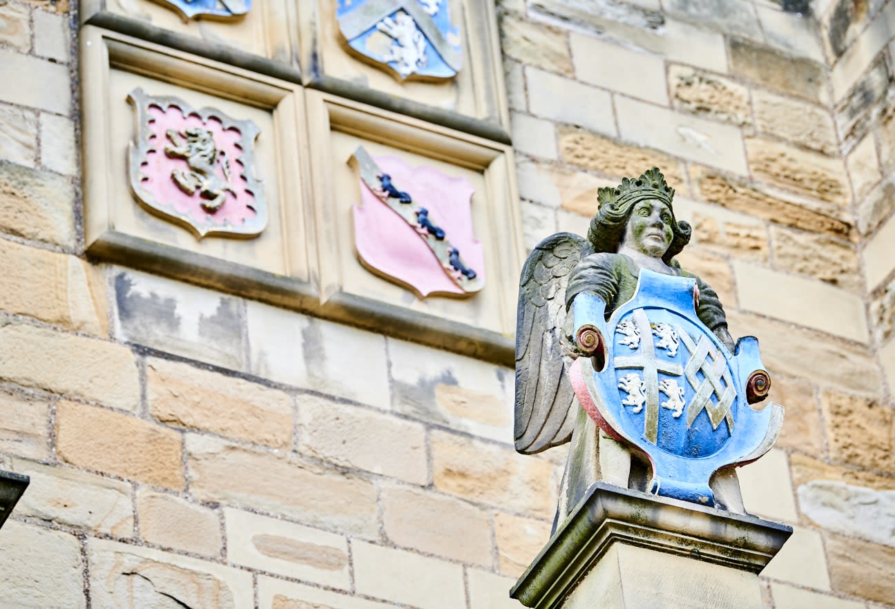 An exterior view of Durham Castle, showing a carving of a crowned figure, displaying the blue and gold crest of Bishop Cosin