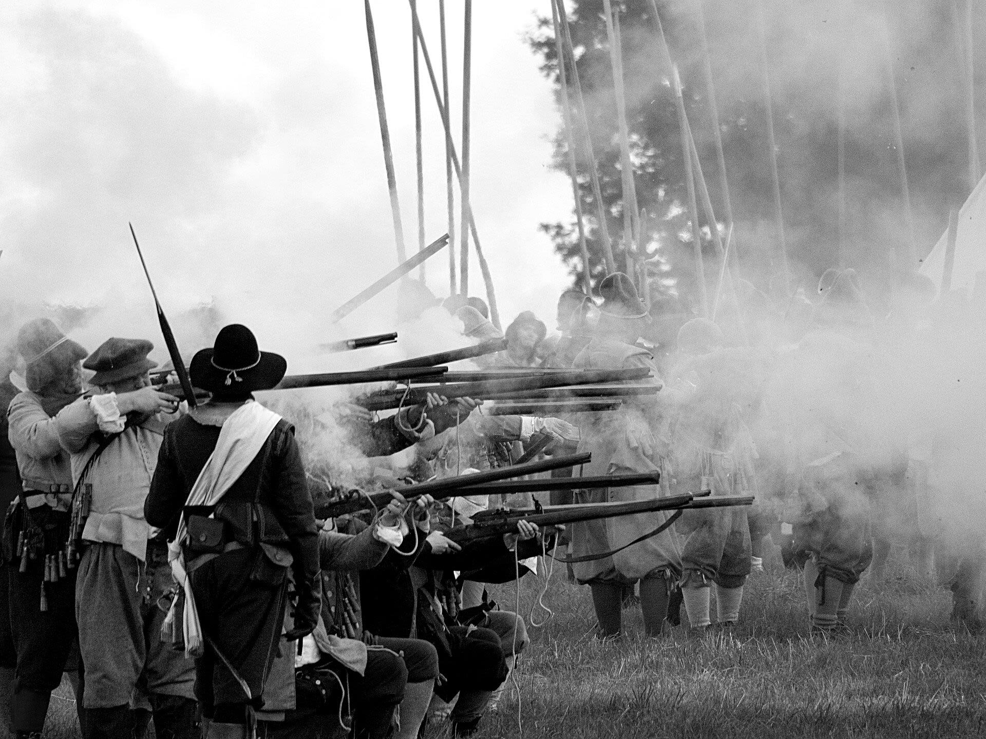 Photo of a Civil War battle reconstruction. A group of soldiers point and fire their muskets, with smoke flying up into the air