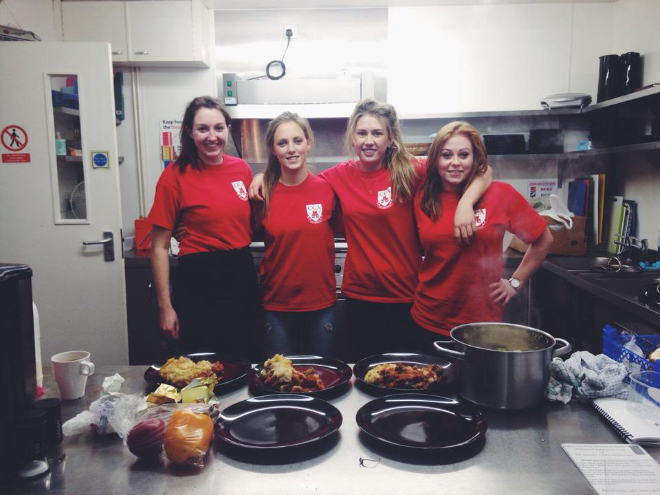 four women students link arms in a kitchen