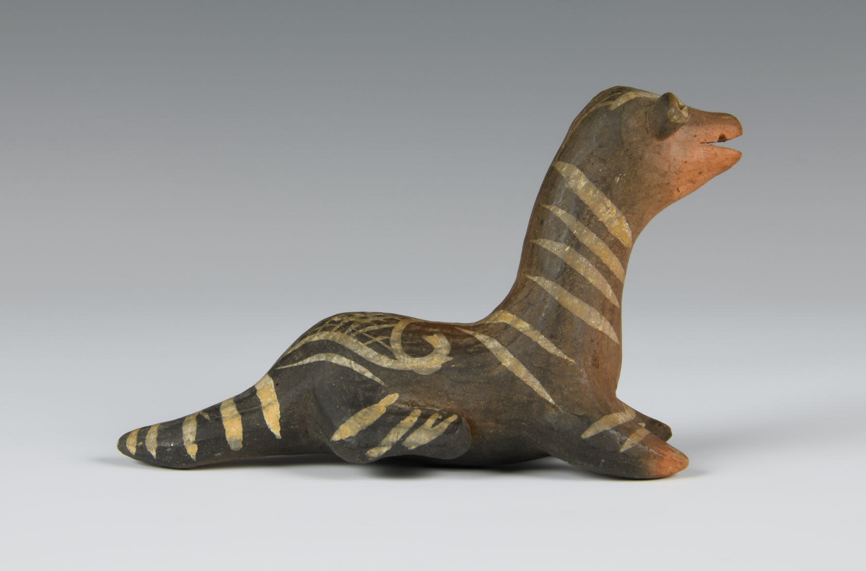 Animal clay toy lying on the ground. The figure is dark brown and has geometric white patterns.