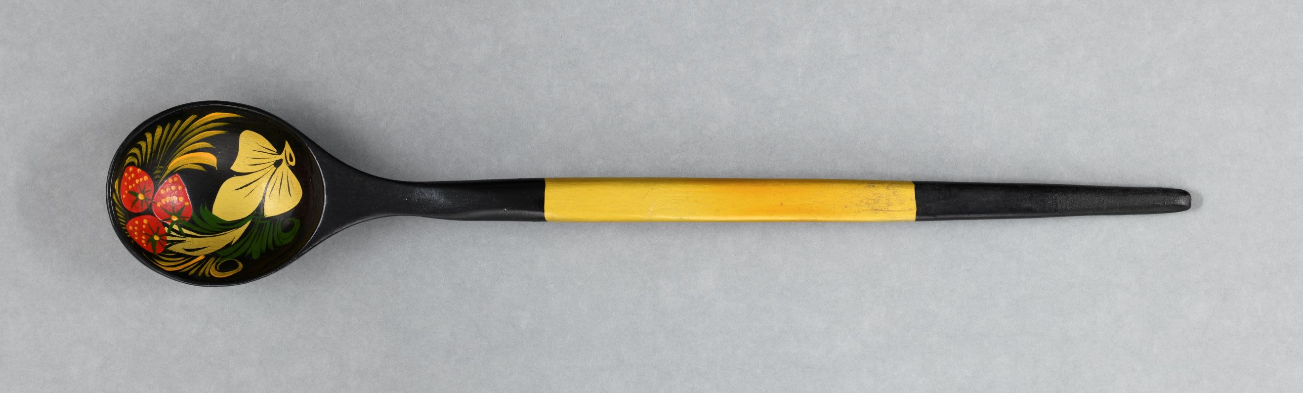 Khokhloma spoon. Lacquered wooden spoon has shallow rounded bowl and a long circular handle is decorated in combination of gold, black, red, green and yellow colours, with strawberries.