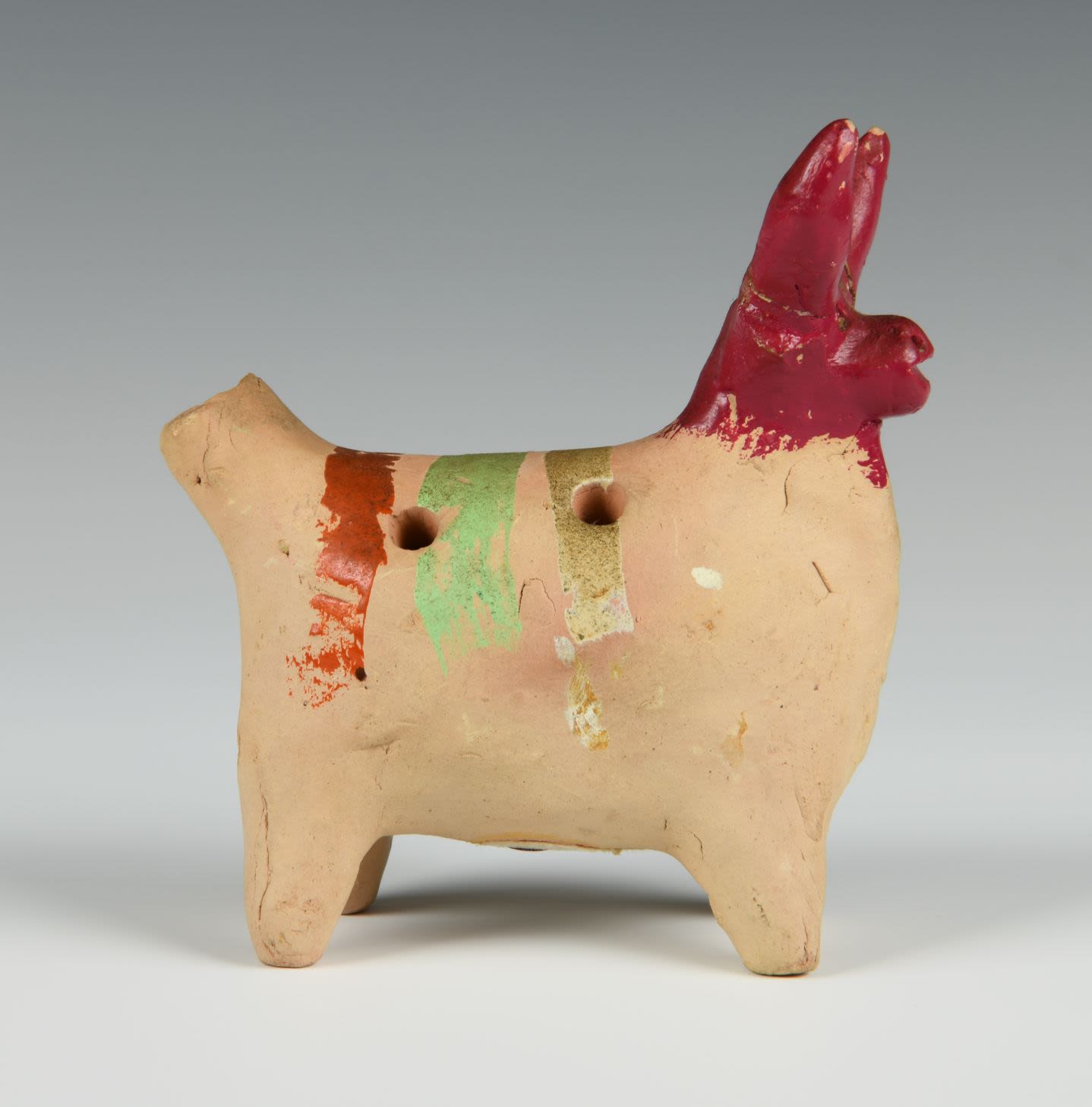 A clay whistle in the shape of a cow with red horns and three stripes on its back in orange, green and gold.