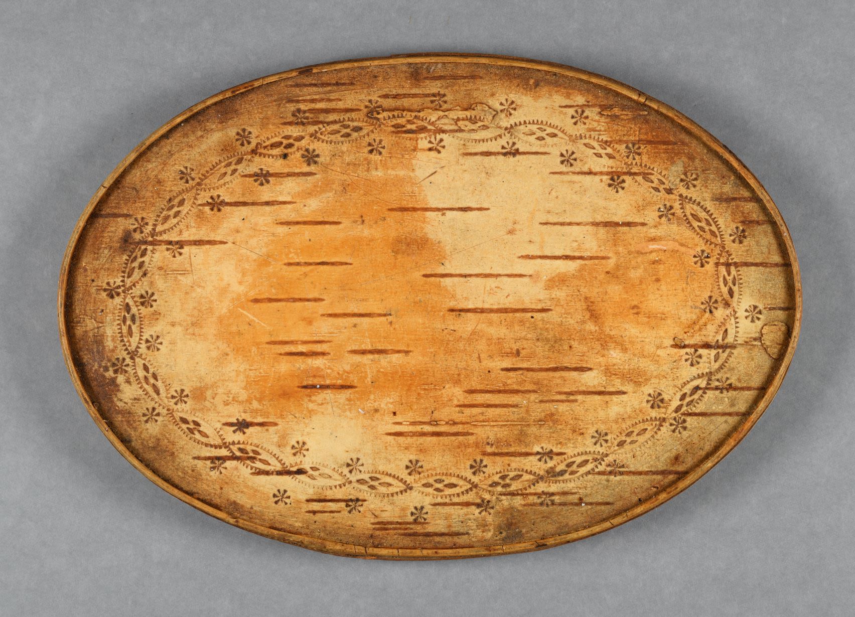 Oval tray made of birch bark with decorative patterns.