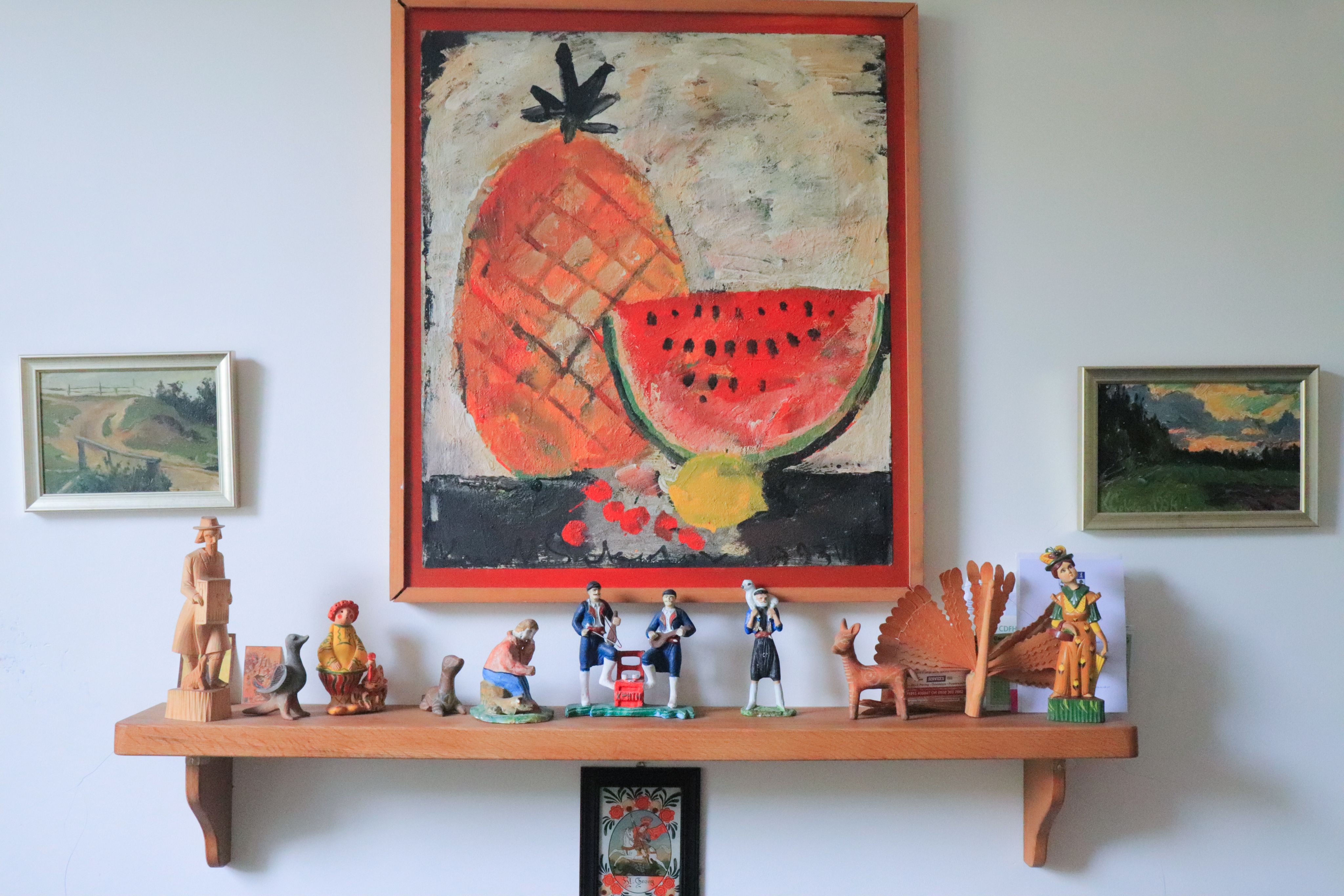 Photograph of figures on a wooden stand and paintings on the wall.