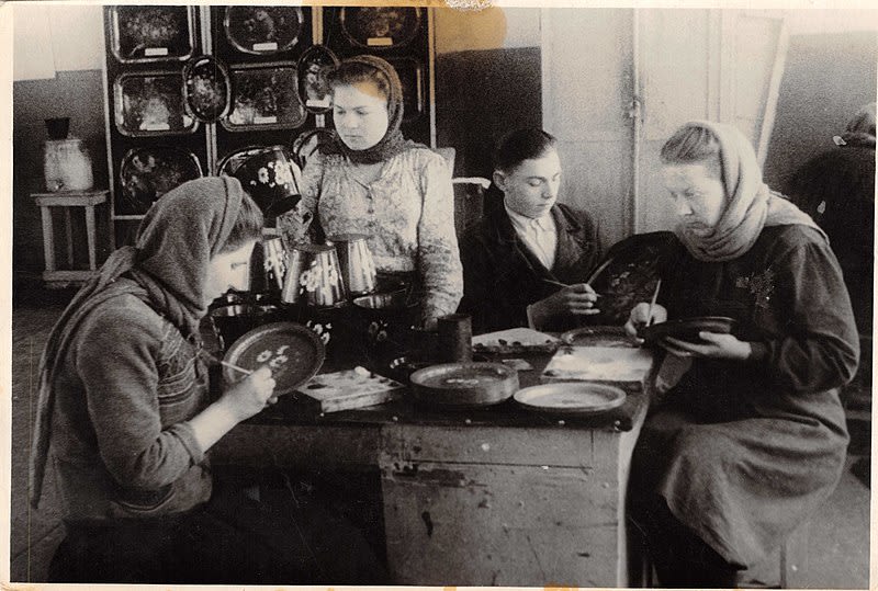 Black and white photograph of people painting floral patterns on trays.