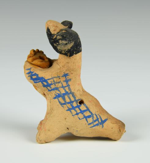 Clay whistle toy depicting a ram. The figure is seated on two short back legs with hoofs and wide elongated tail which is shaped as a mouthpiece for the whistle with one hole at the top of the tail, next one in a buttock area. It is unpainted but haas blue rectangular patterns and a grey head.