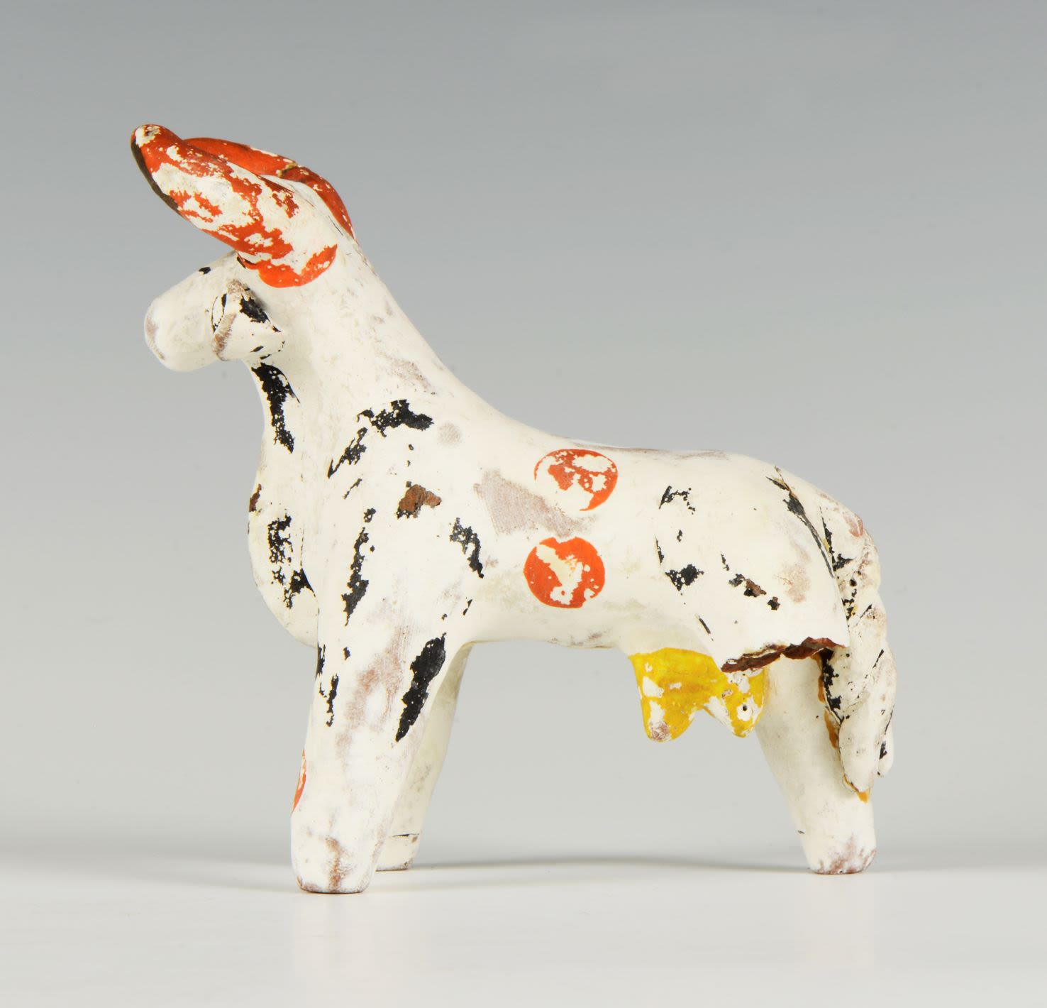 White clay toy of a cow decorated with orange, yellow, brown and green patterns.