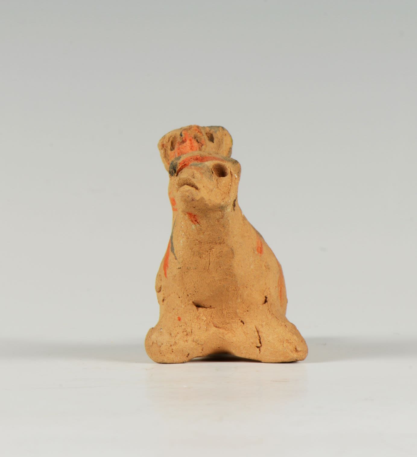 Small animal object made of clay that stands on two wings. It is roughly decorated with orange and grey lines.