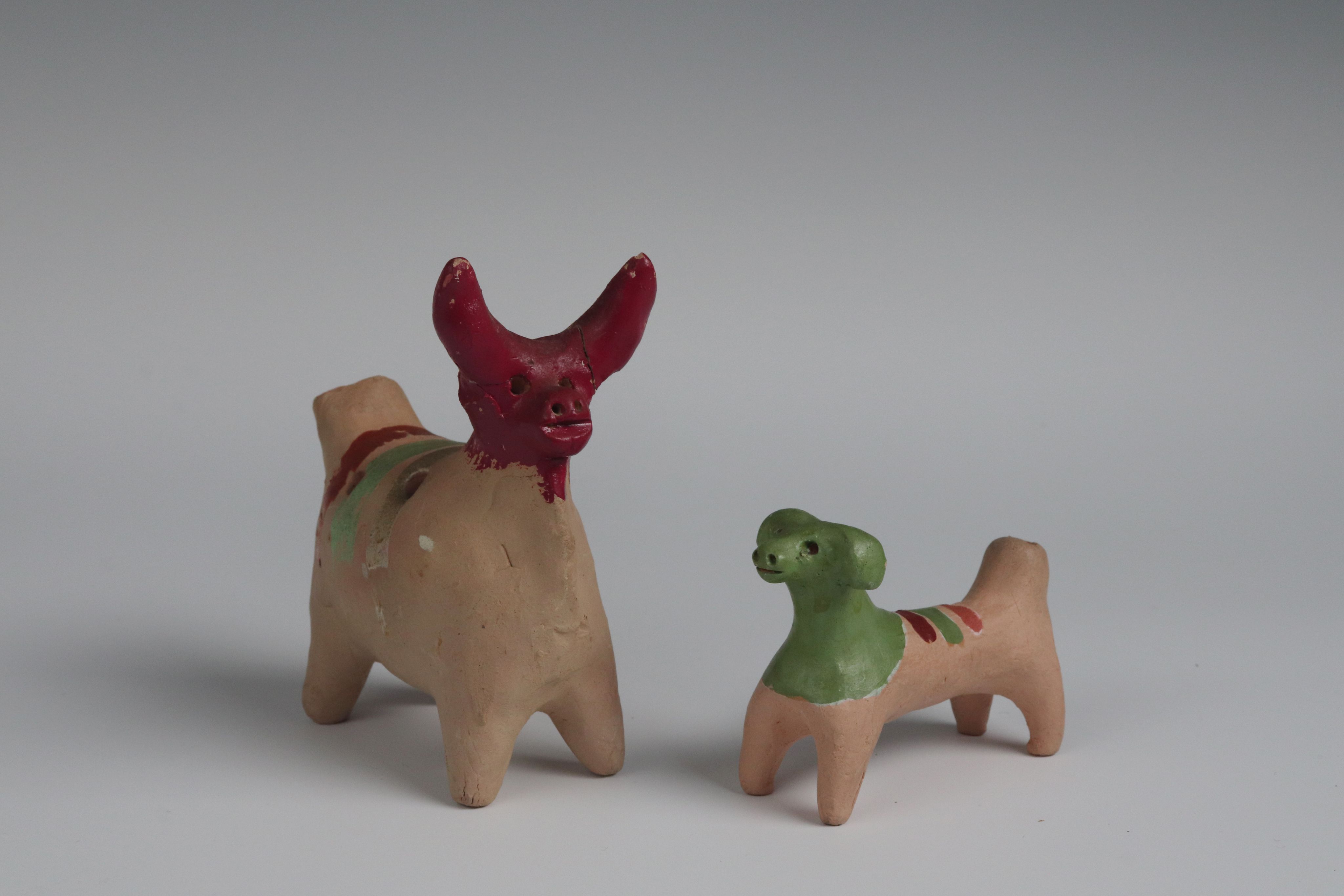 small clay toys: a dog and a cow. the faces are painted respectively green and red with coloured stripes on their backs.