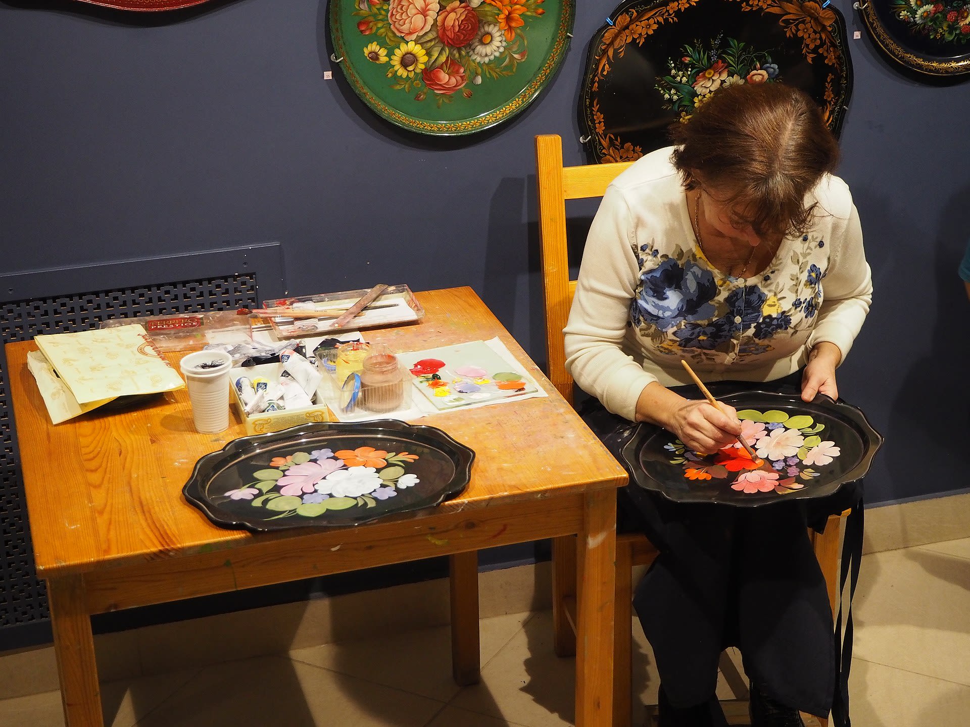 Woman painting floral patterns on tray.