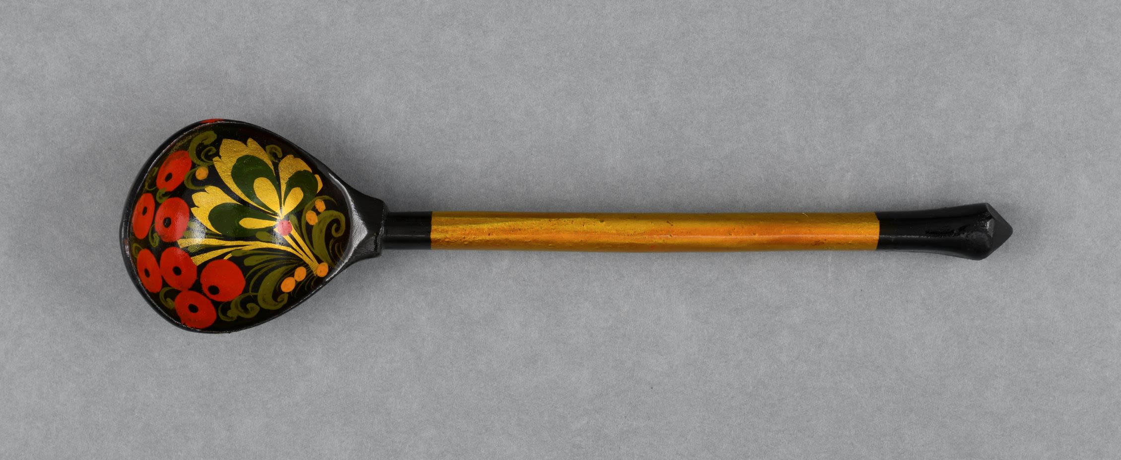 Lacquered wooden spoon with deep rounded bowl decorated with gold, black, red, yellow and green paint. Handle of the spoon is gold with a black tip.