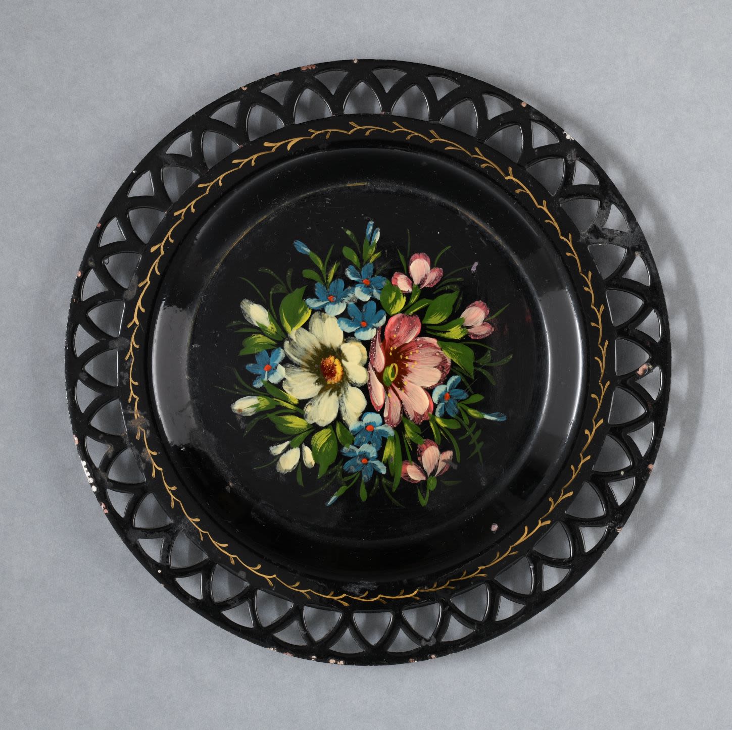 Zhostovo painted lacquer tray-plate. The circular black tray with openwork rim trimmed with gold twig like pattern. The centre of the tray is decorated with a bouquet of flowers in rich vivid colours of blue, white, red, yellow and pink with green leaves which is the most widely used motif of the Zhostovo painting. The floral ornament is completed in traditional manner without using stencils or outlines.