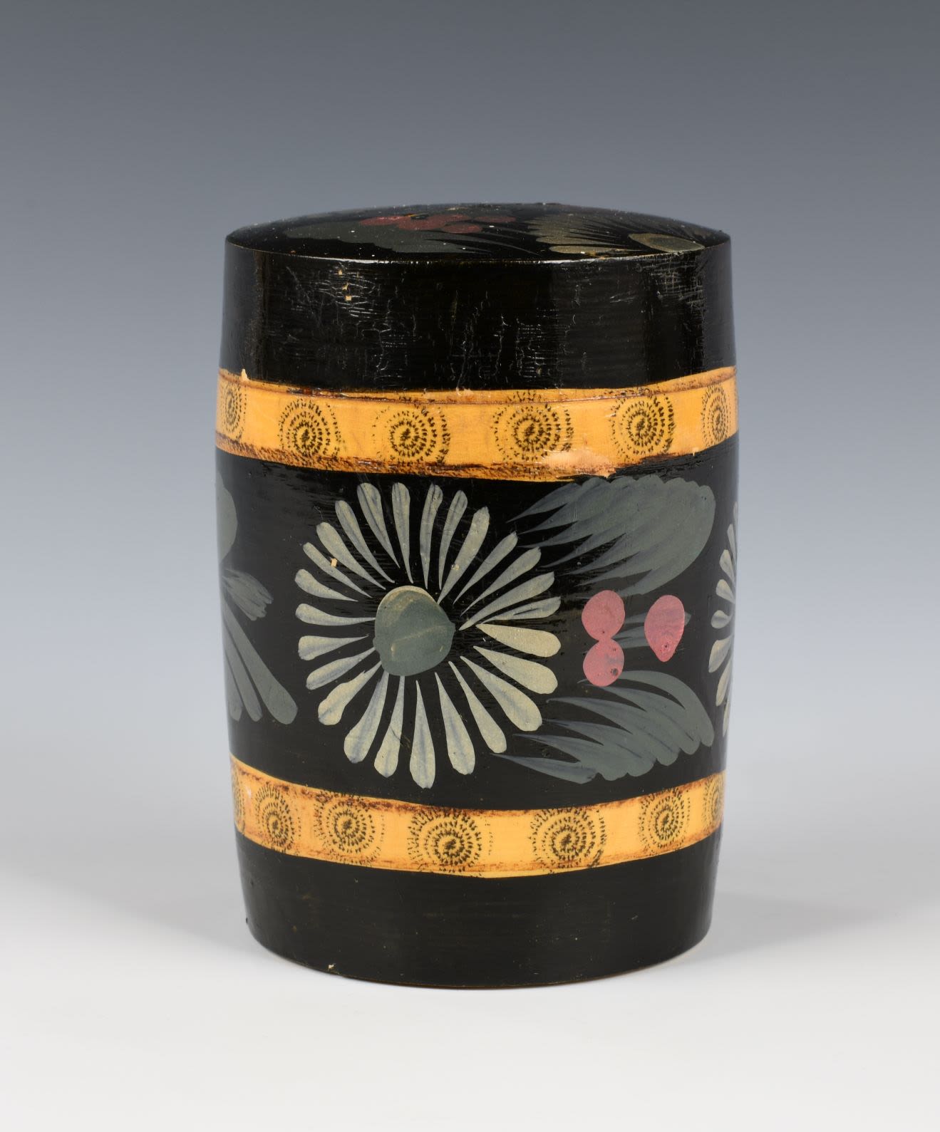 Lacquer wooden jar with a lid in the shape of a barrel with floral pattern. It has a yellow stripe with a pattern of spirals made of black dots at the bottom and top. There is a slit in the top which could be for money.