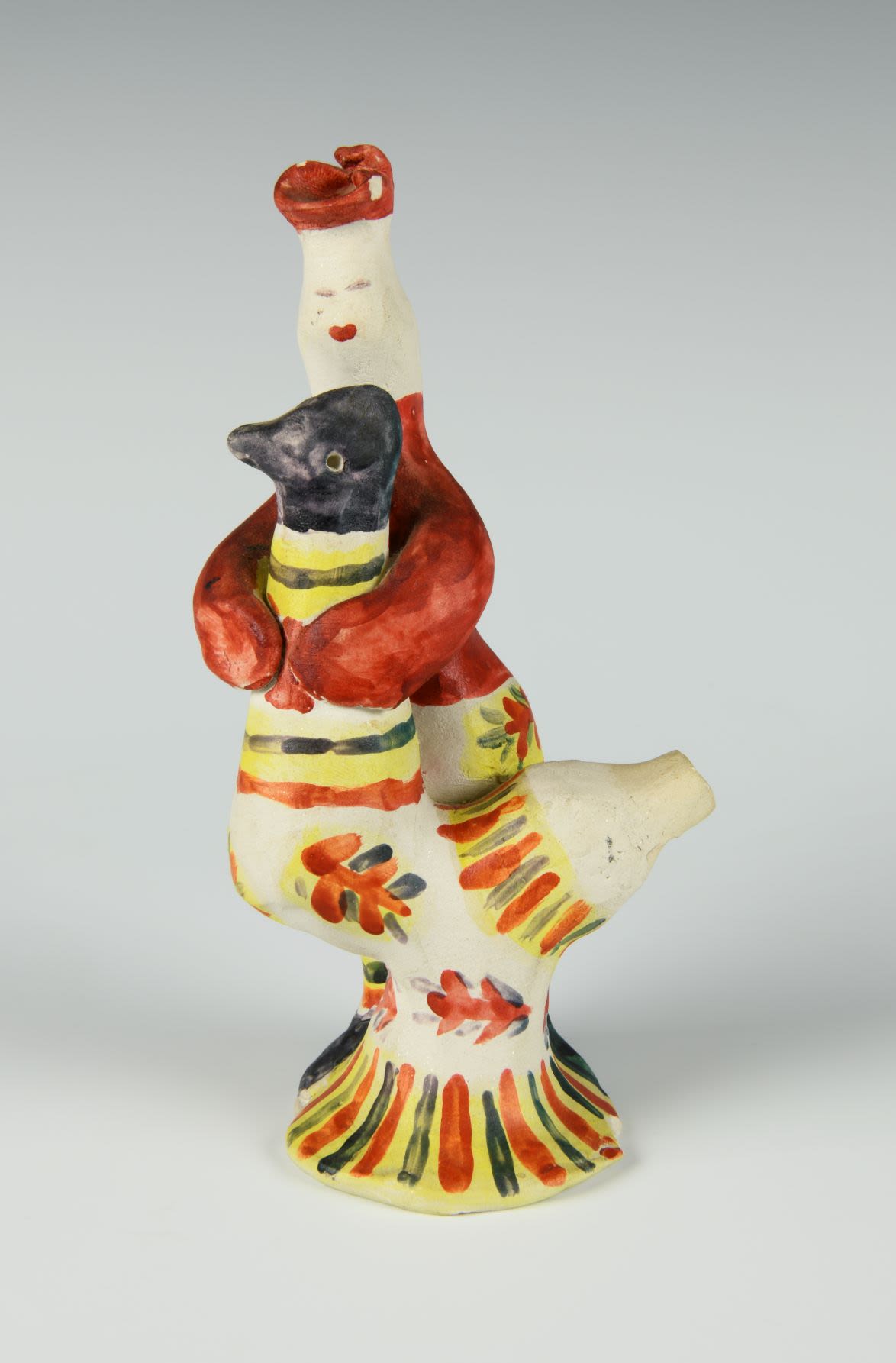 Clay toy of a figure hugging a large hen. The figure wears a red shirt and had, and the hen has a black head and stripes in red, green, and black on its body and food pedestal.