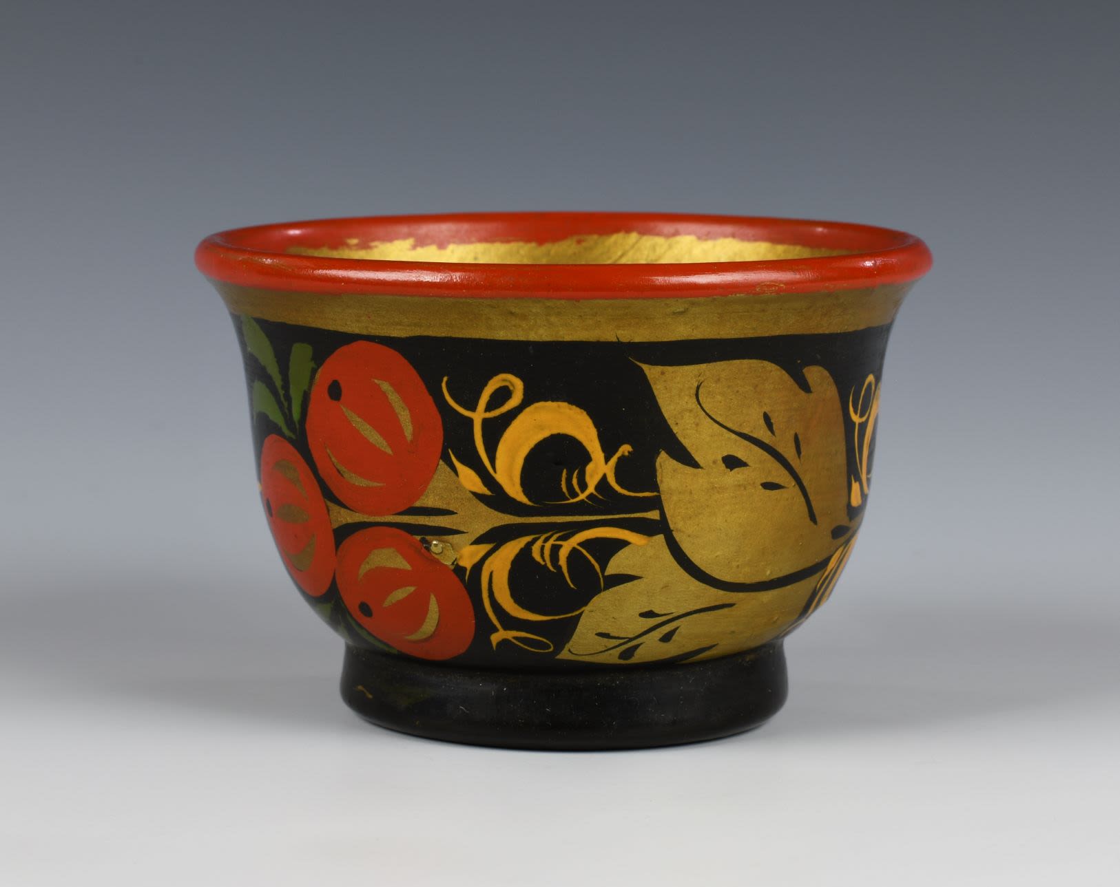 Lacquer wooden cup with a red rim and gold inside. Outside of the cup decorated with a repeating design of a cluster of three red Rowan berries and two golden leafs with green and yellow grass elements on a black background.