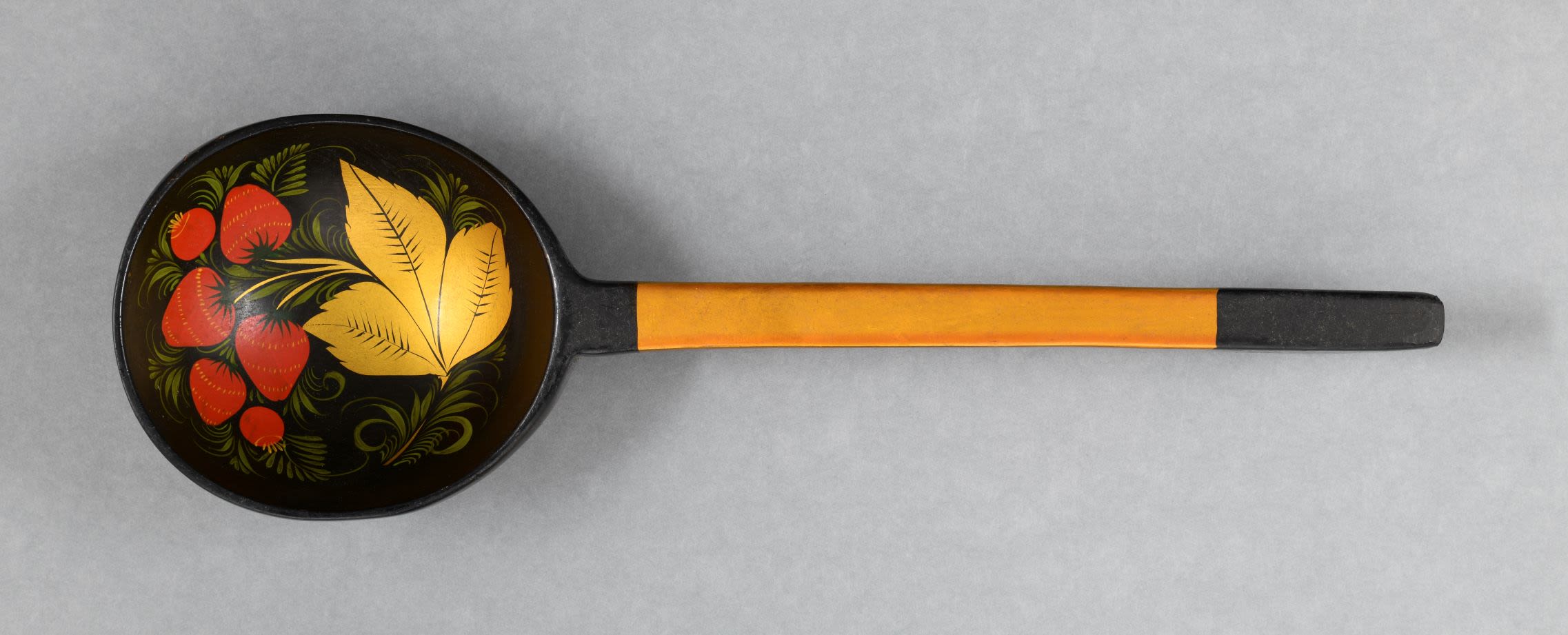 Lacquered wooden teaspoon with deep rounded bowl and a rectangular handle which has an extended tip is decorated in combination of gold, black, red, green and yellow colours. Handle of the ladle is gold with black tip. The black bowl with a cluster of red strawberries with yellow achenes interwoven with gold trefoil leaf, green grasses and tendrils from both sides.