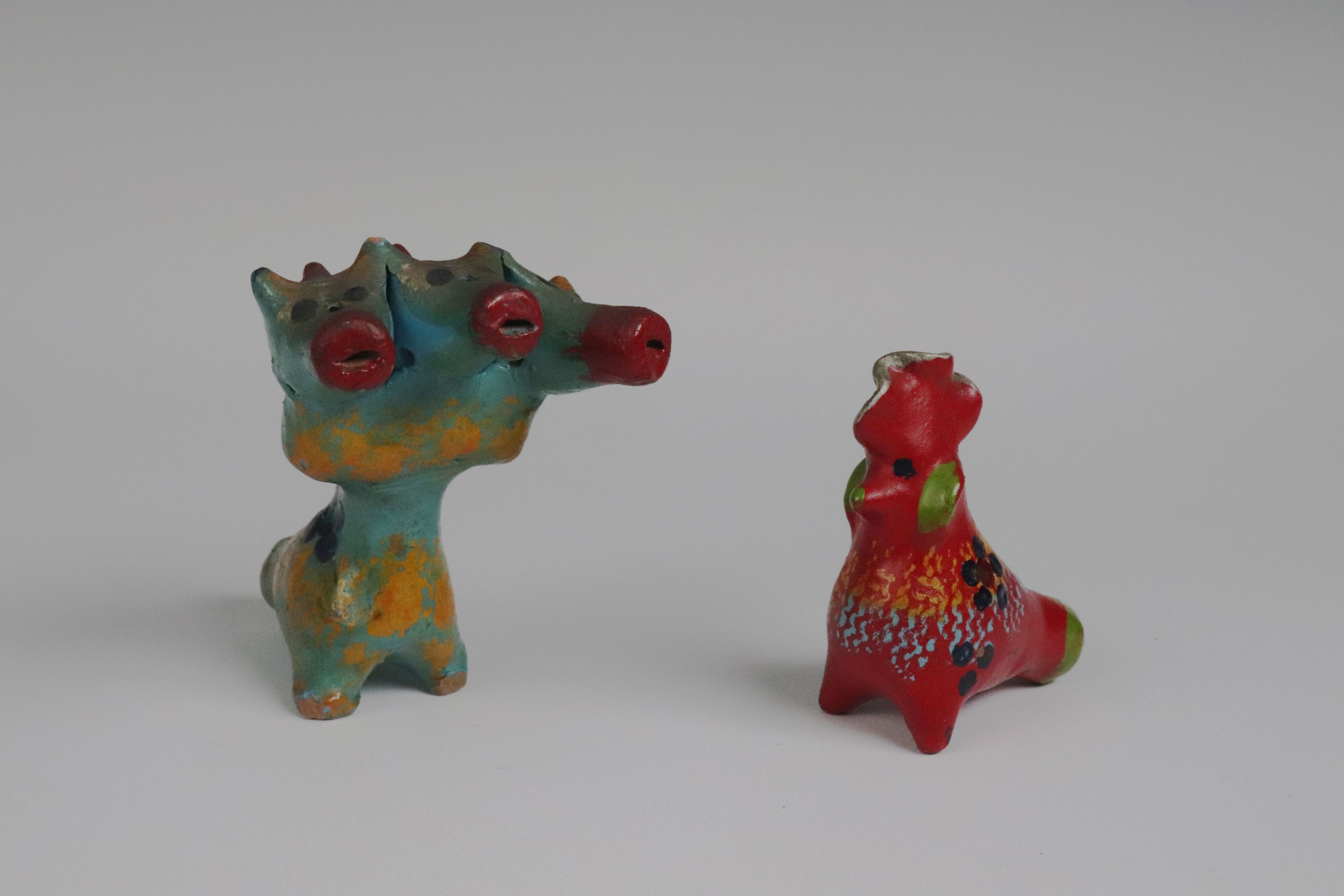 two clay toys depicting a fantastic creature or dragon and a cockerel decorated with lively colours